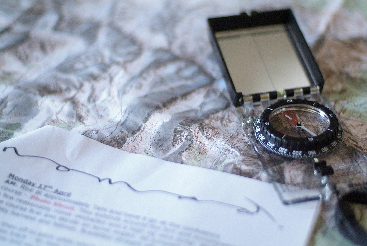 A baseplate compass laying on a map with Nomad paperwork