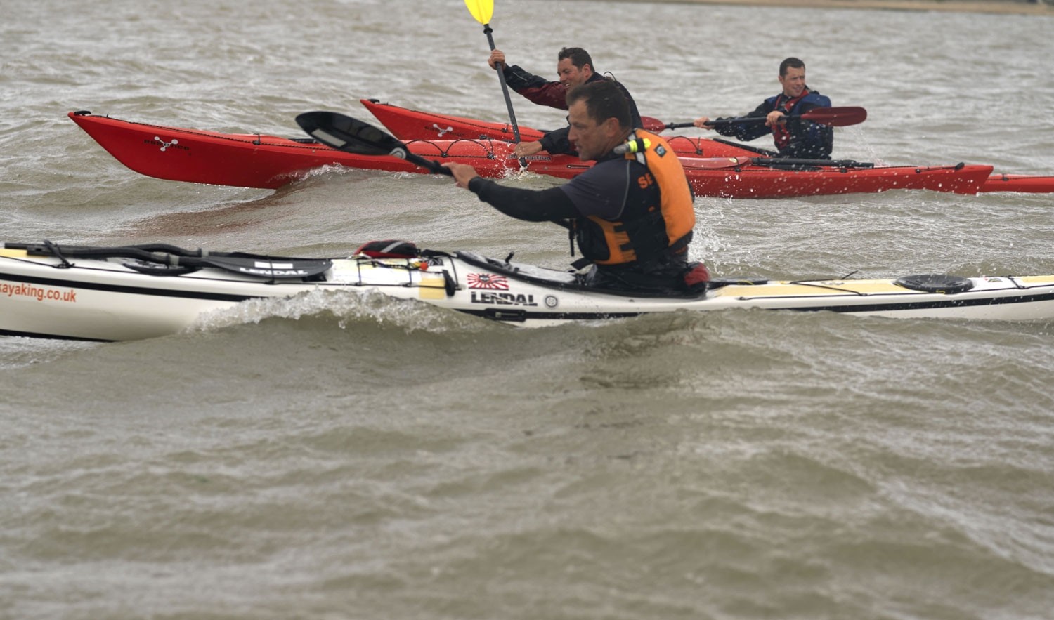 Three sea kayakers paddling hard alongside each other off Brightlingsea in Essex
