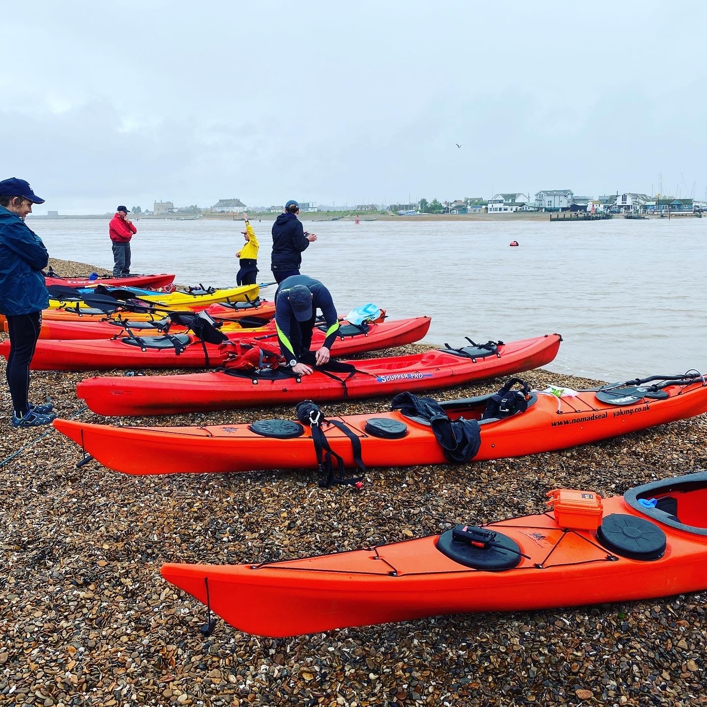 Red & orange kayaks on a shingle beach in Suffolk with NOMAD Sea Kayaking.