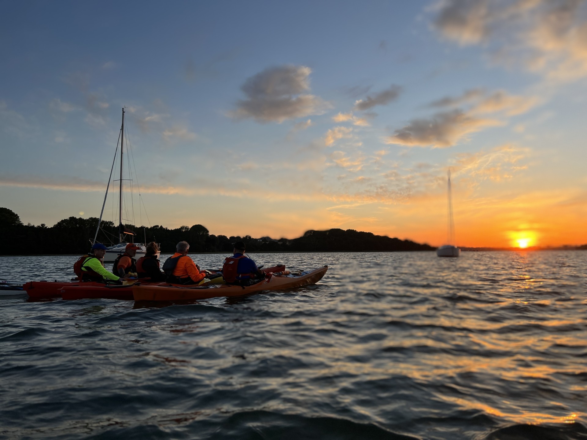 Group of sea kayakers rafted & watching sunset in the distance.