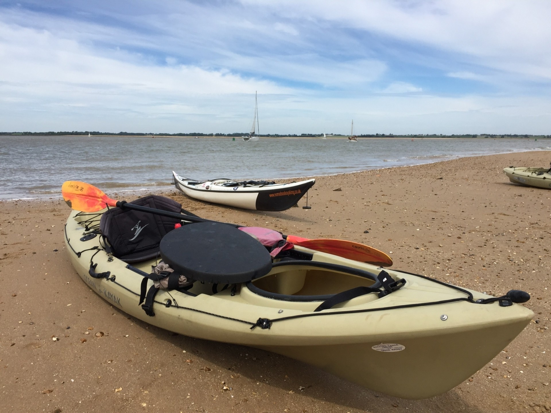 Two Kayaks on the beach with a yacht on the water in the background
