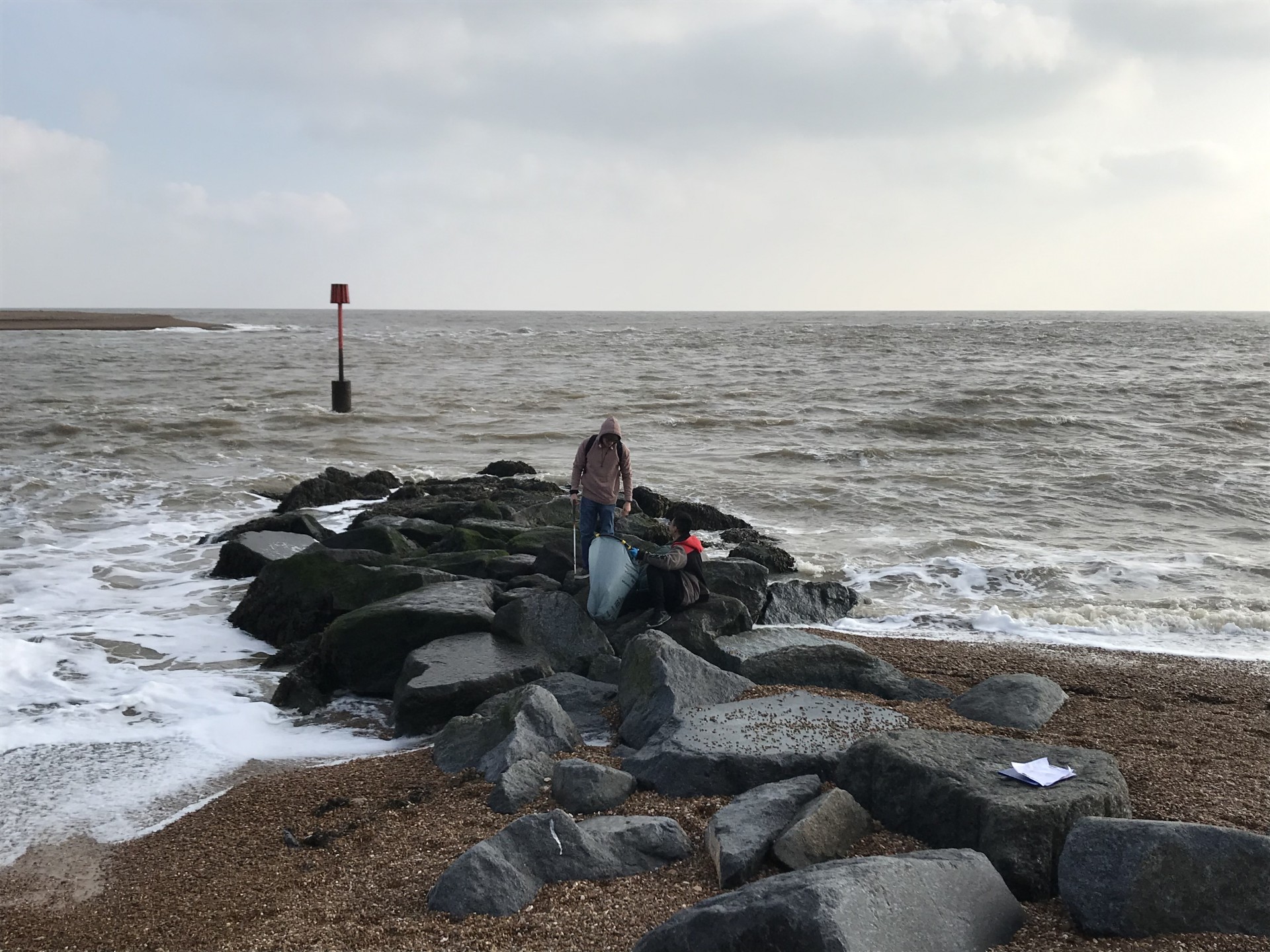 A litter picker with a bag picking up plastic litter at Felixstowe Ferry