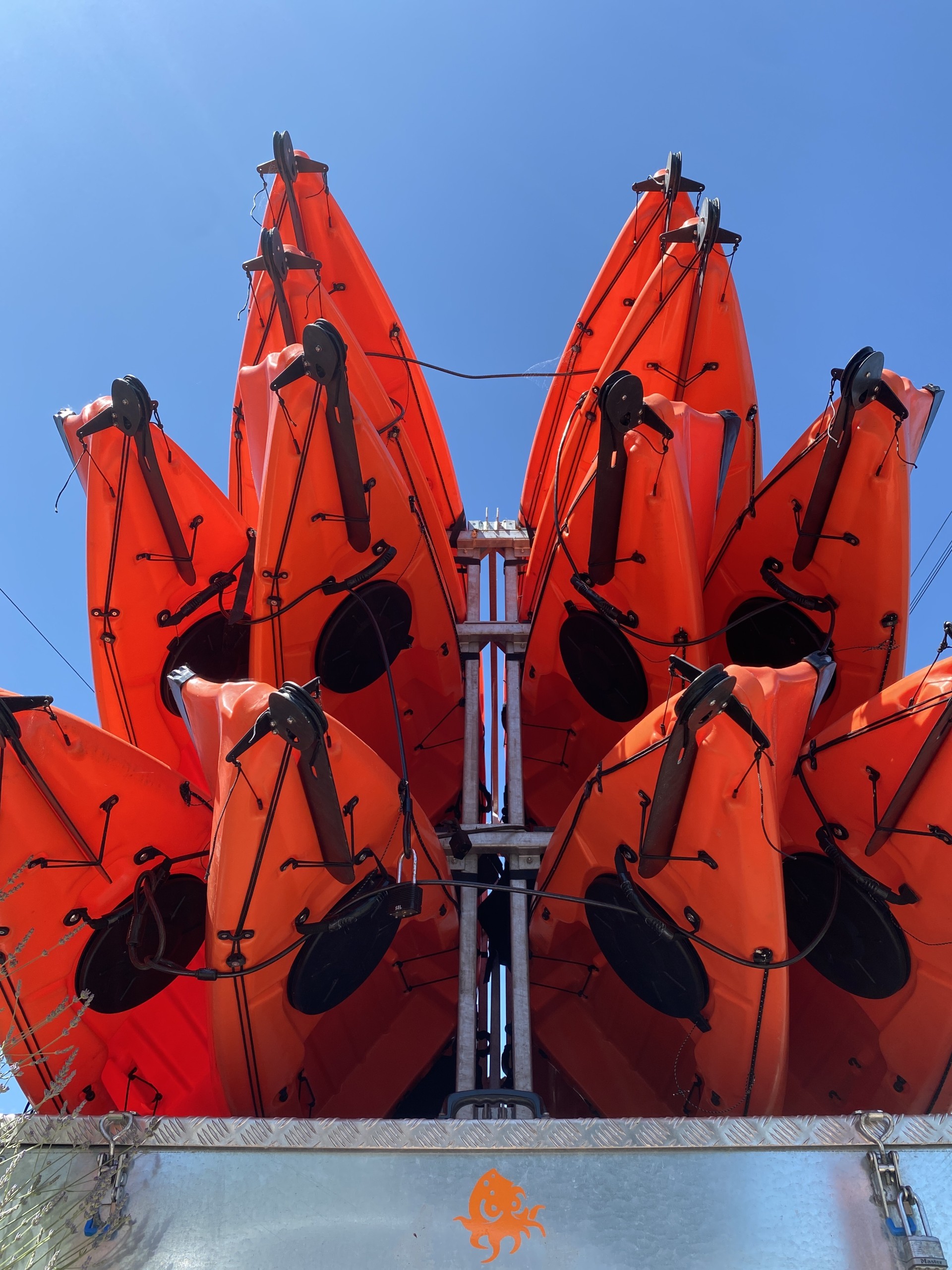 Orange sit-on-top kayaks on a trailer with NOMAD Sea Kayaking.