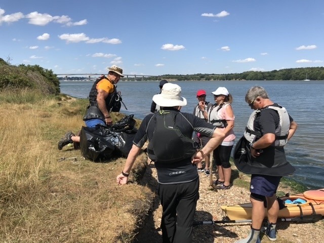 Group on a beach with the Orwell bridge in the far distance whilst beach cleaning by kayak