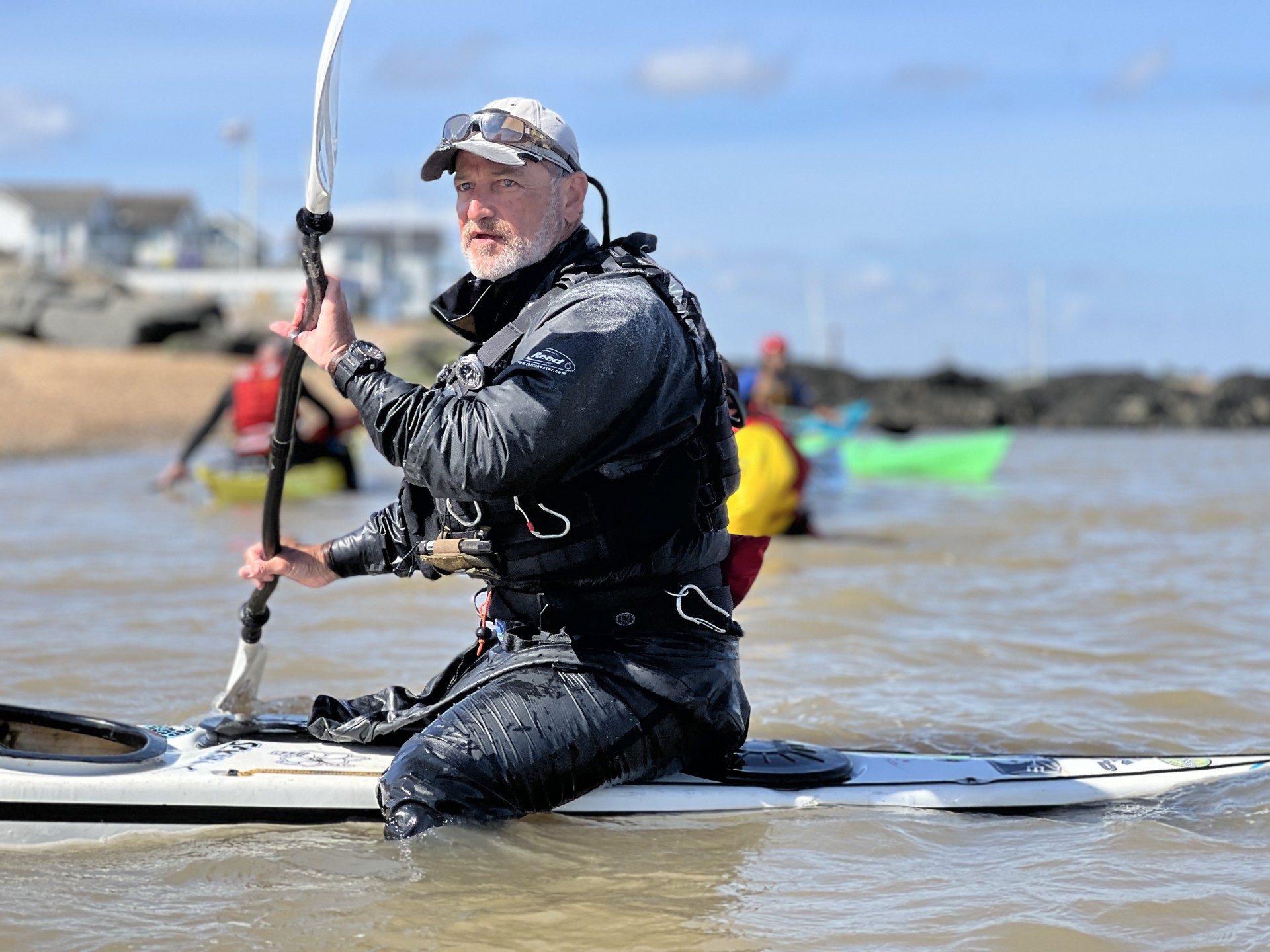 A sea kayaker balancing on the back deck of his kayak dressed in a drysuit.