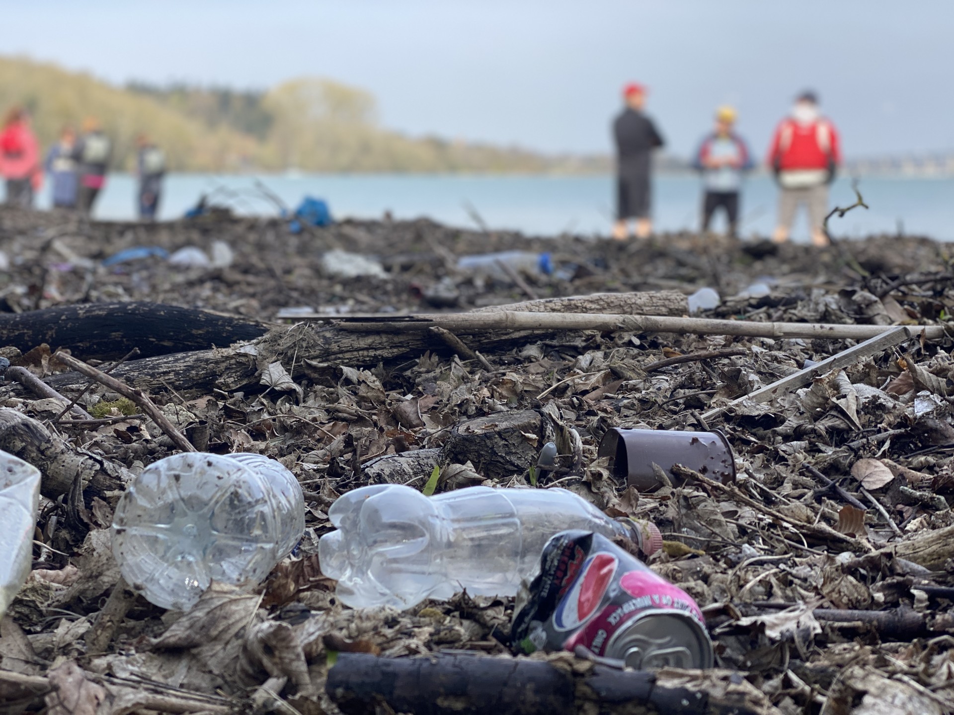 Plastic bottles and tins lying on a beach with kayakers in the background.