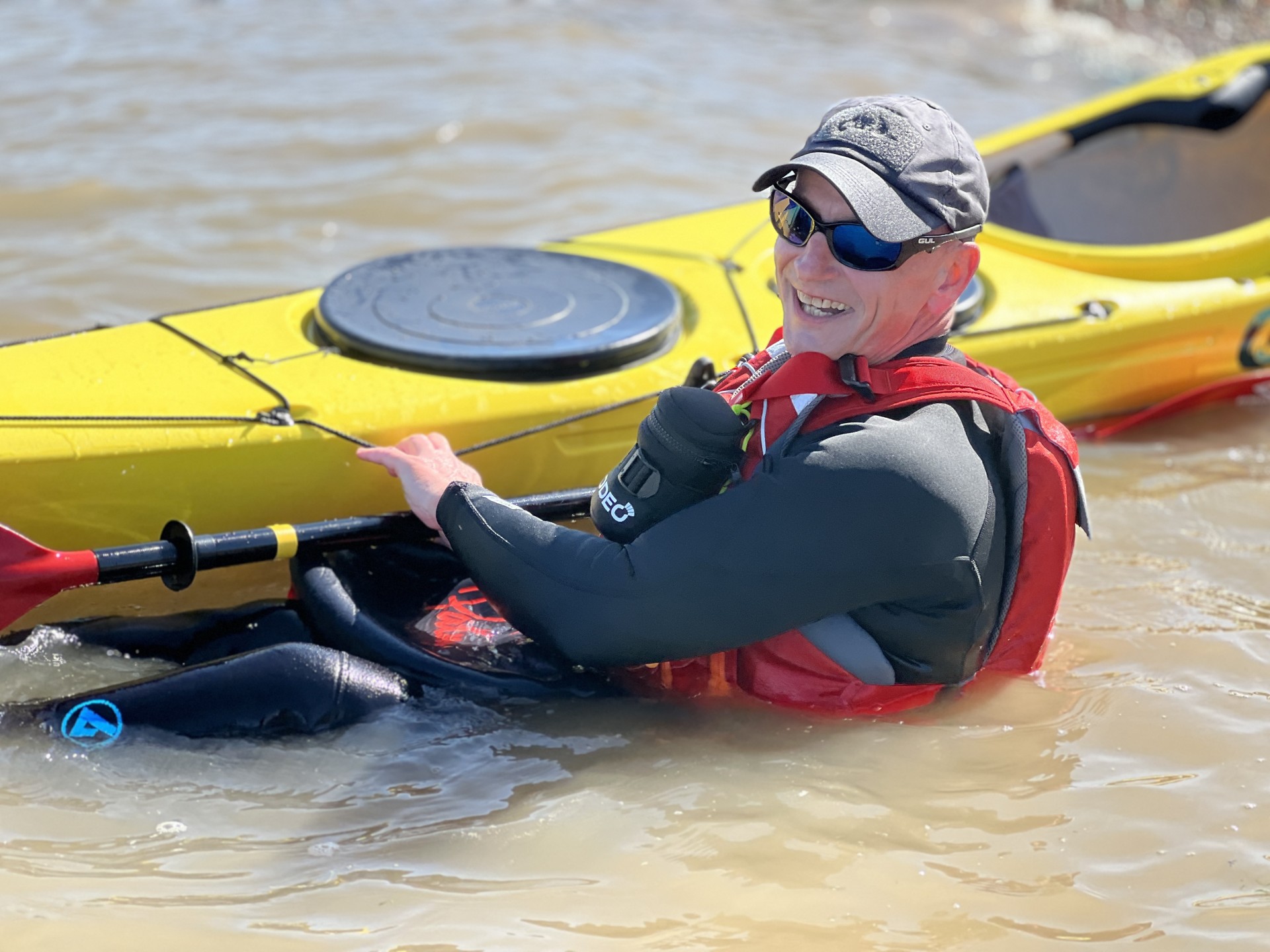 Smiling kayakers in the water next to his yellow kayak.