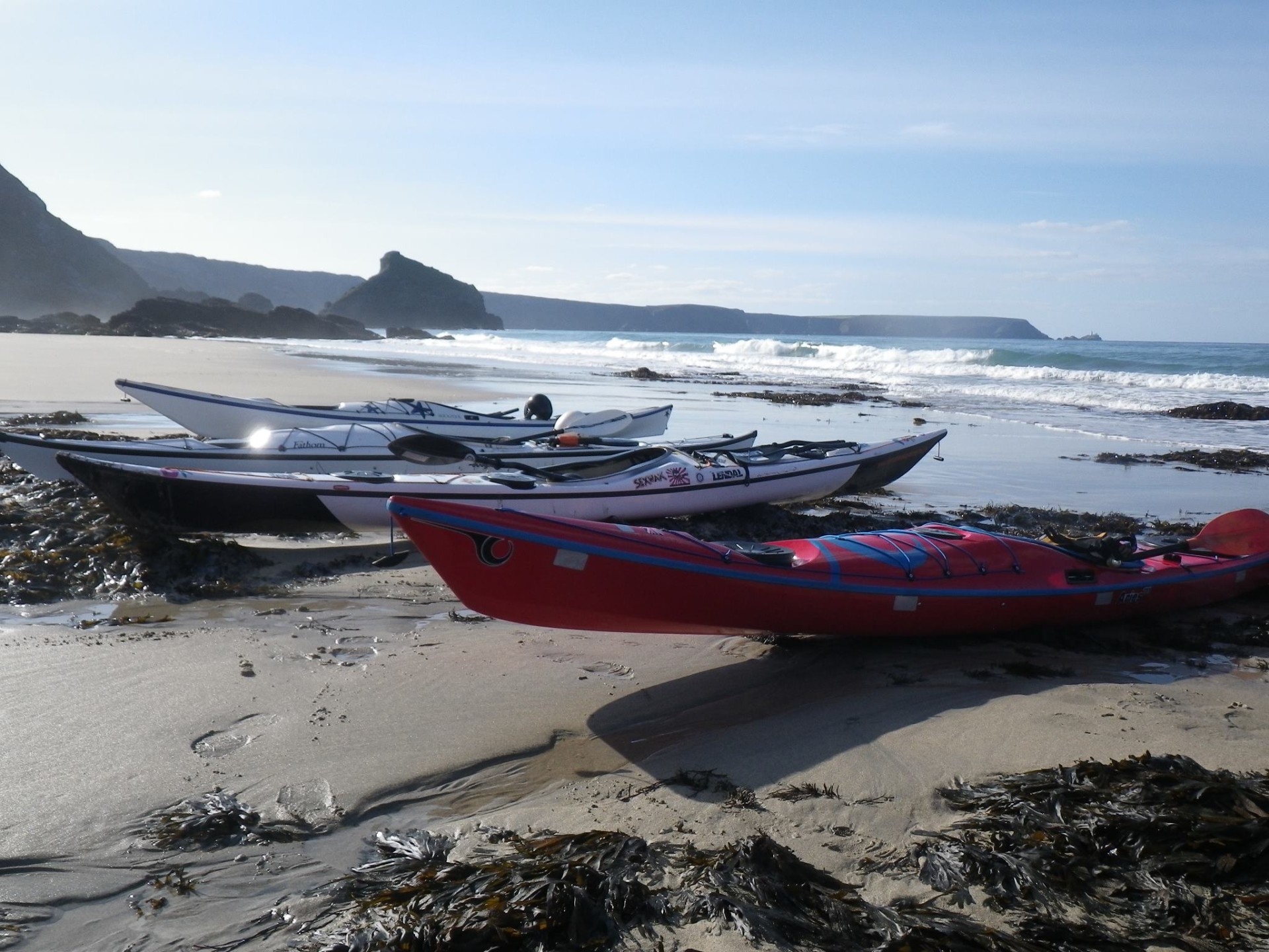 Sea kayaks on a Cornish beach on a sunny summers day with NOMAD Sea Kayaking.