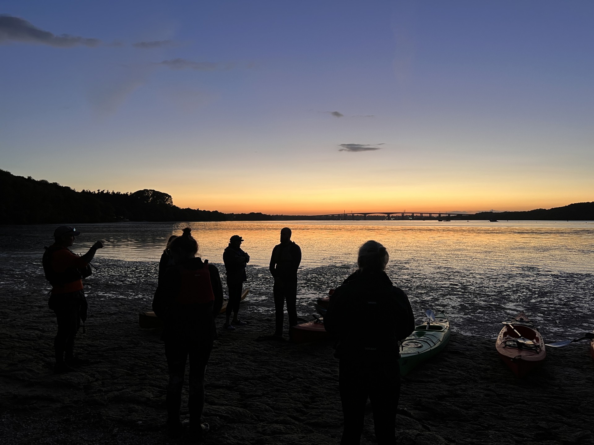 Sea kayakers landing on a beach at sunset.