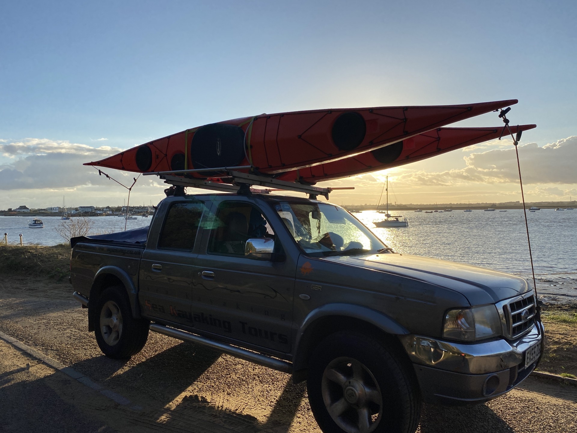 Orange sea kayaks on roof racks with the sun setting in the background.