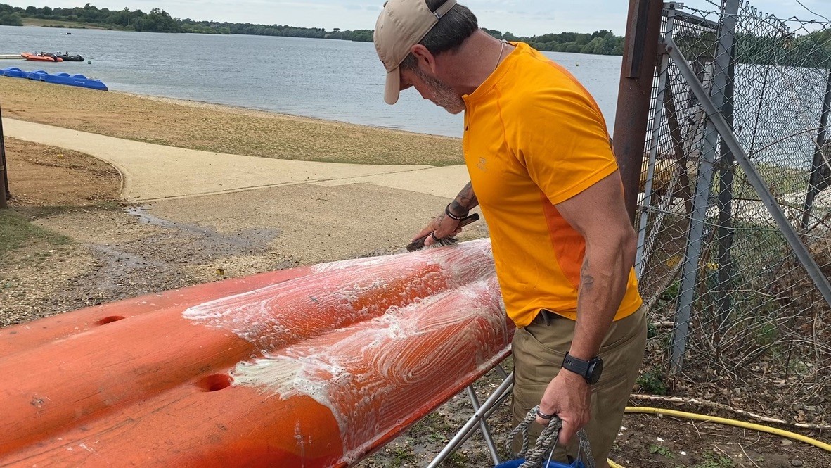 A guide in an orange uniform shirt scrubbing kayaks