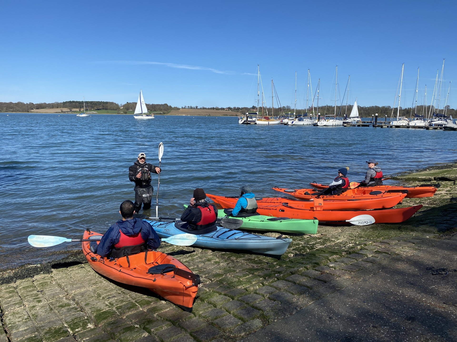 Kayakers preparing to launch kayaks into a blue sea with blues skies in the background.