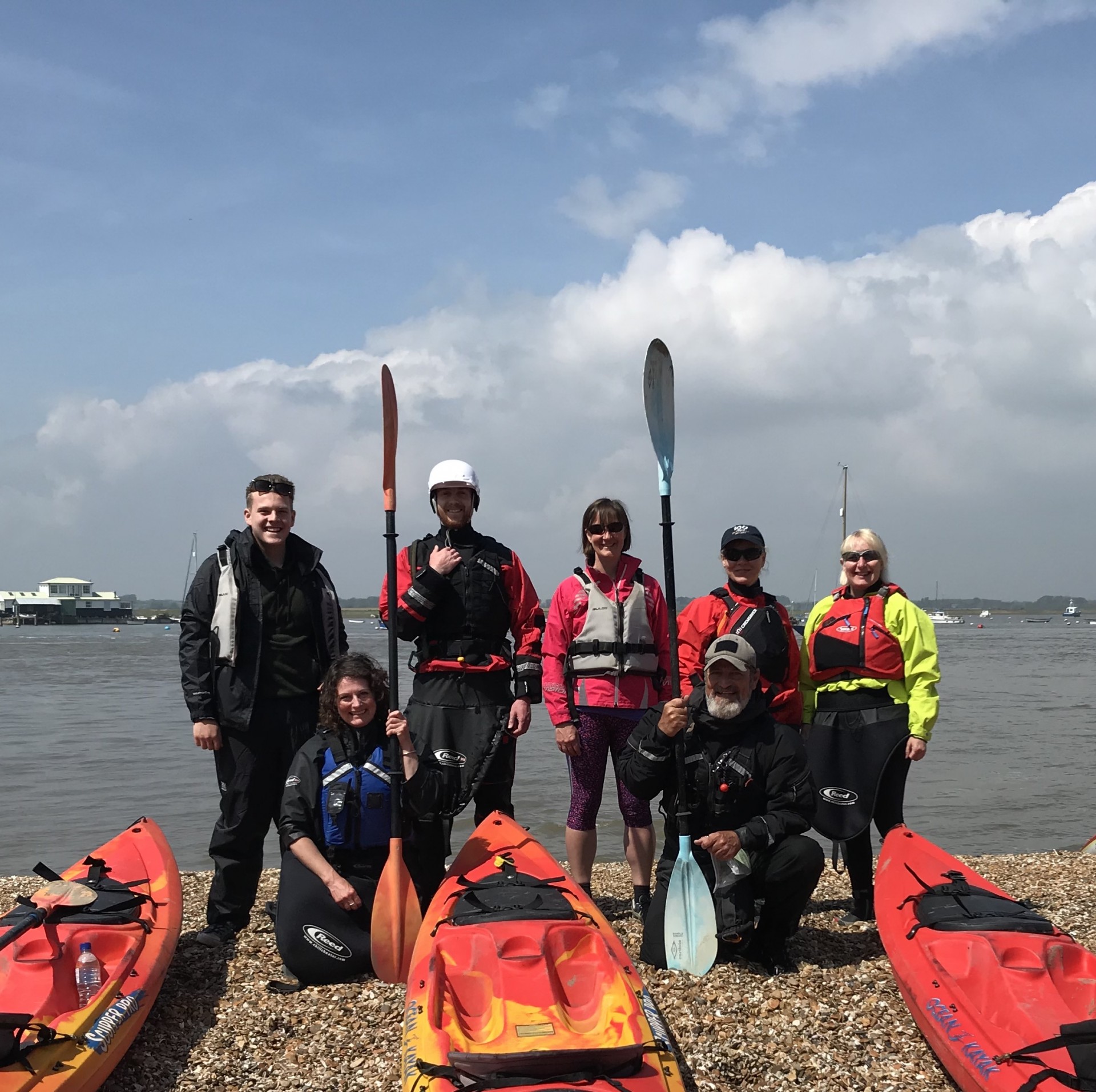 Small group of kayakers posing on a beach with the Deben estuary in the background.