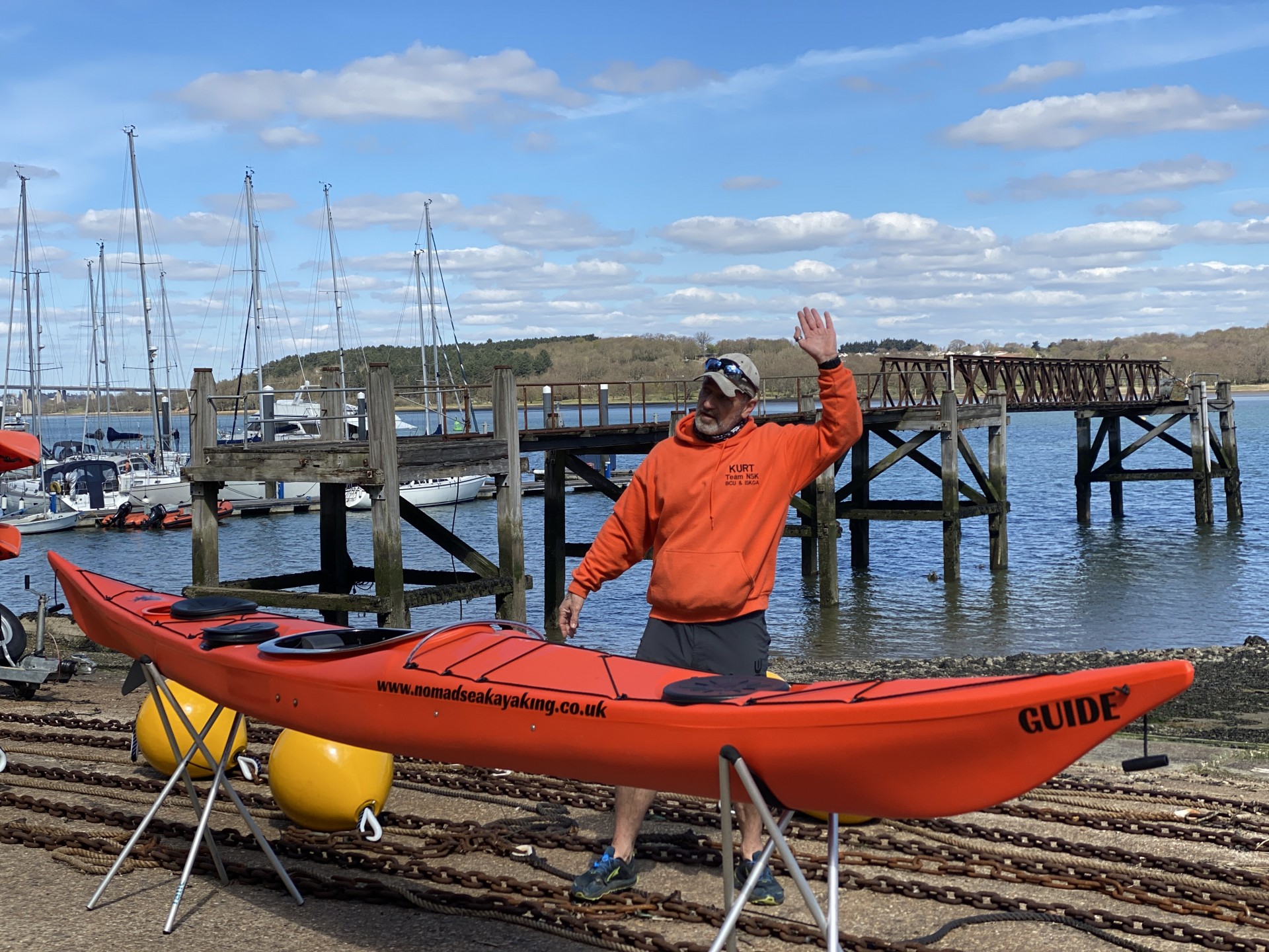 Coaching in an orange top with an orange sea kayak on trestles in front of him.