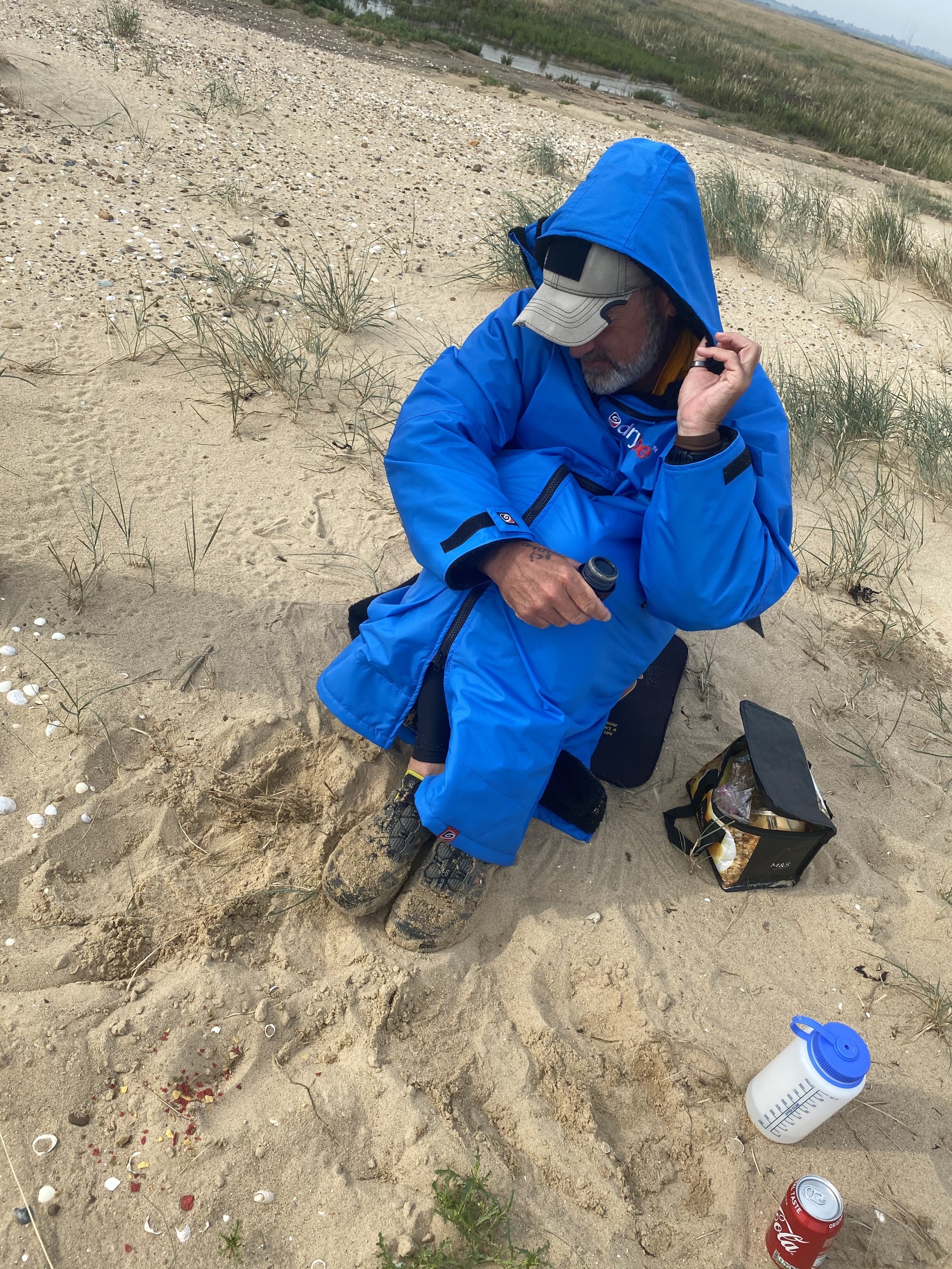 A sea kayak guide on a sandy beach with warm clothing taking a break