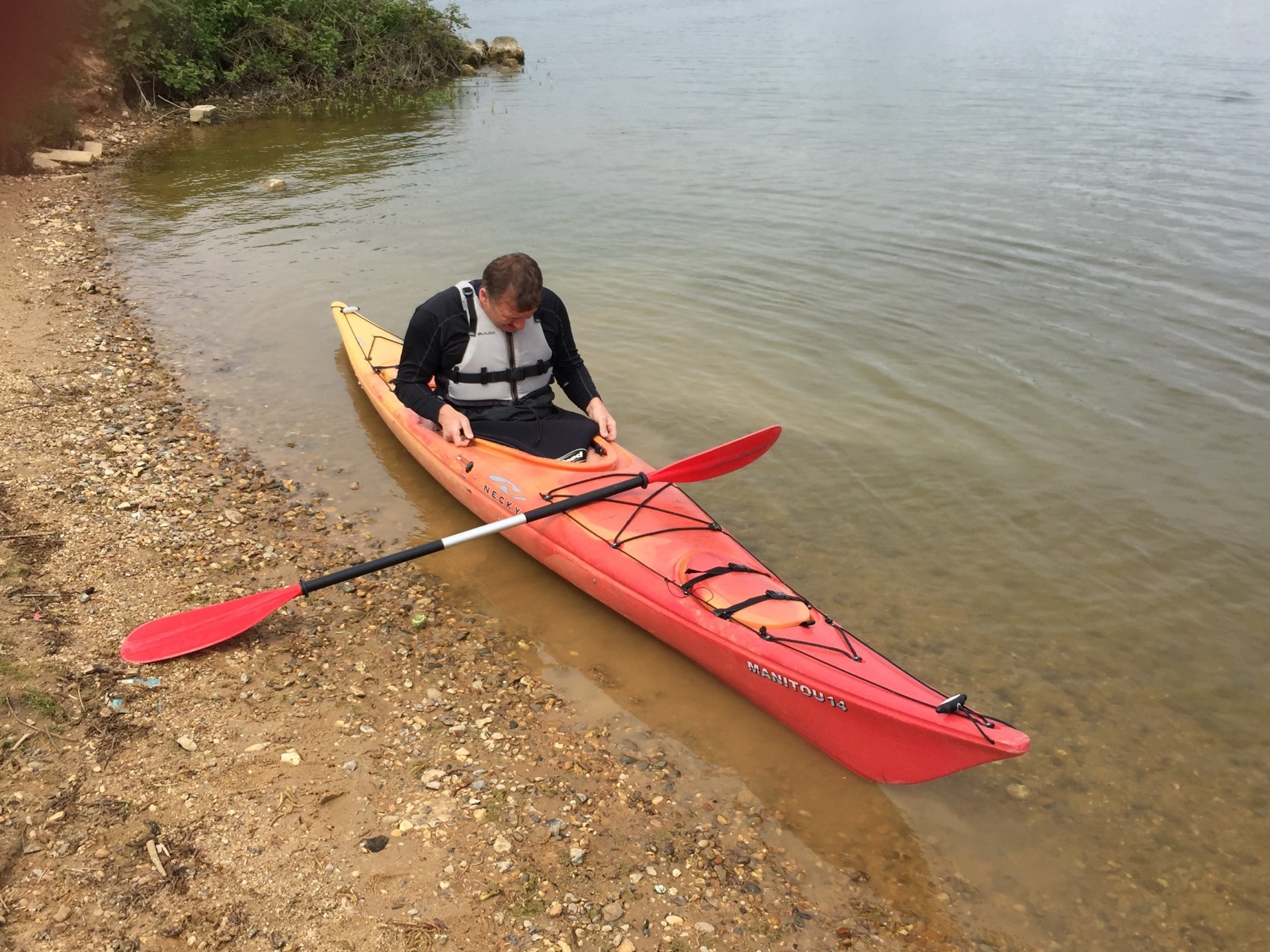 A red touring kayak being launched in flat water
