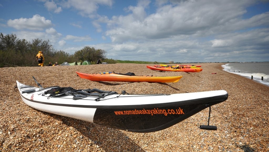 Sea kayaks on the beach with wild camp site in the background.