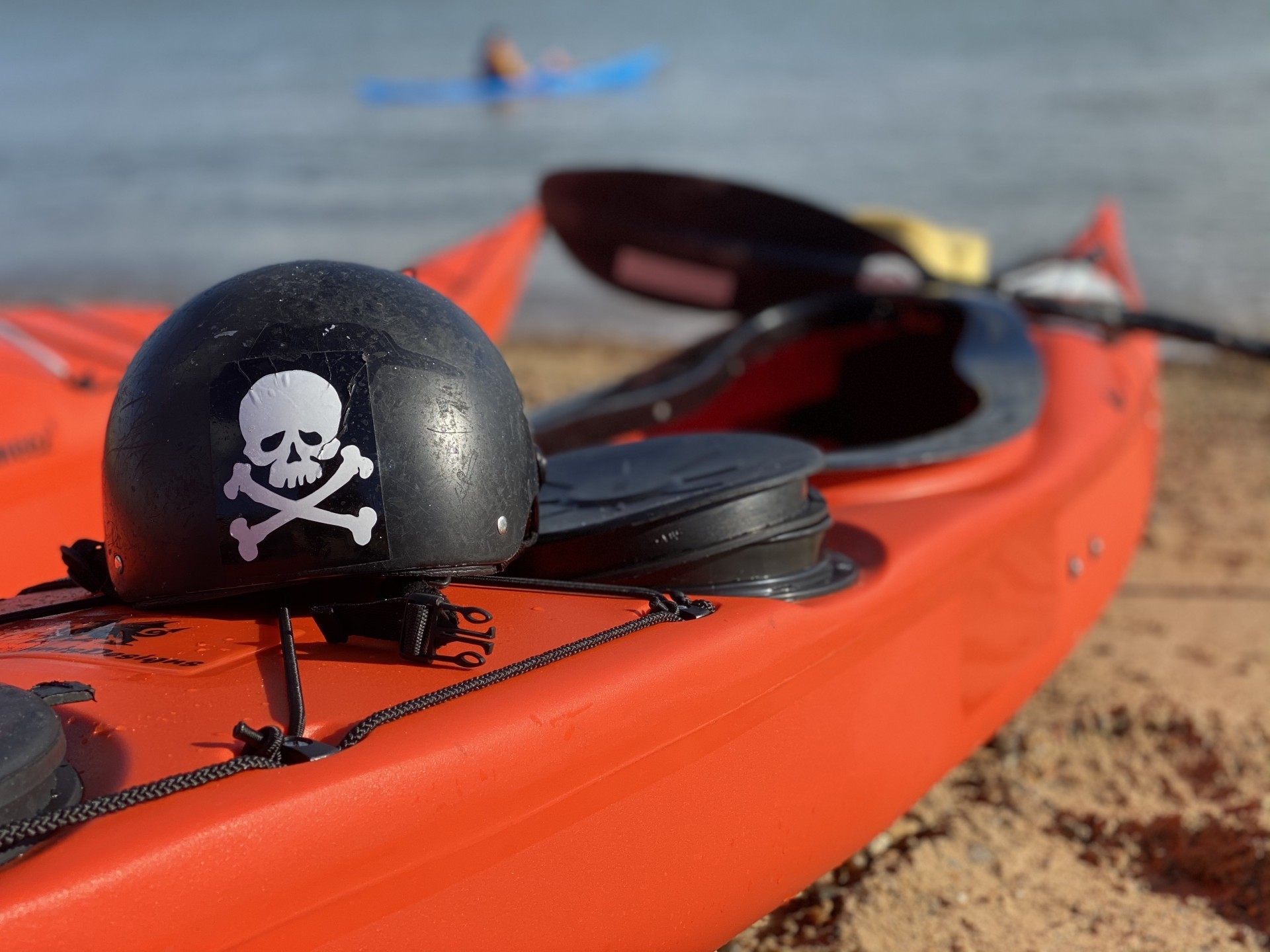Red sea kayaks on a sandy beach with a black helmet lying on the rear deck.