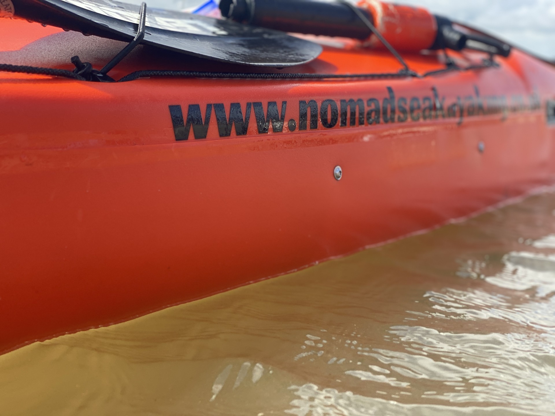 www.nomadseakayaking.co.uk website on the side of a sea kayak on the water.