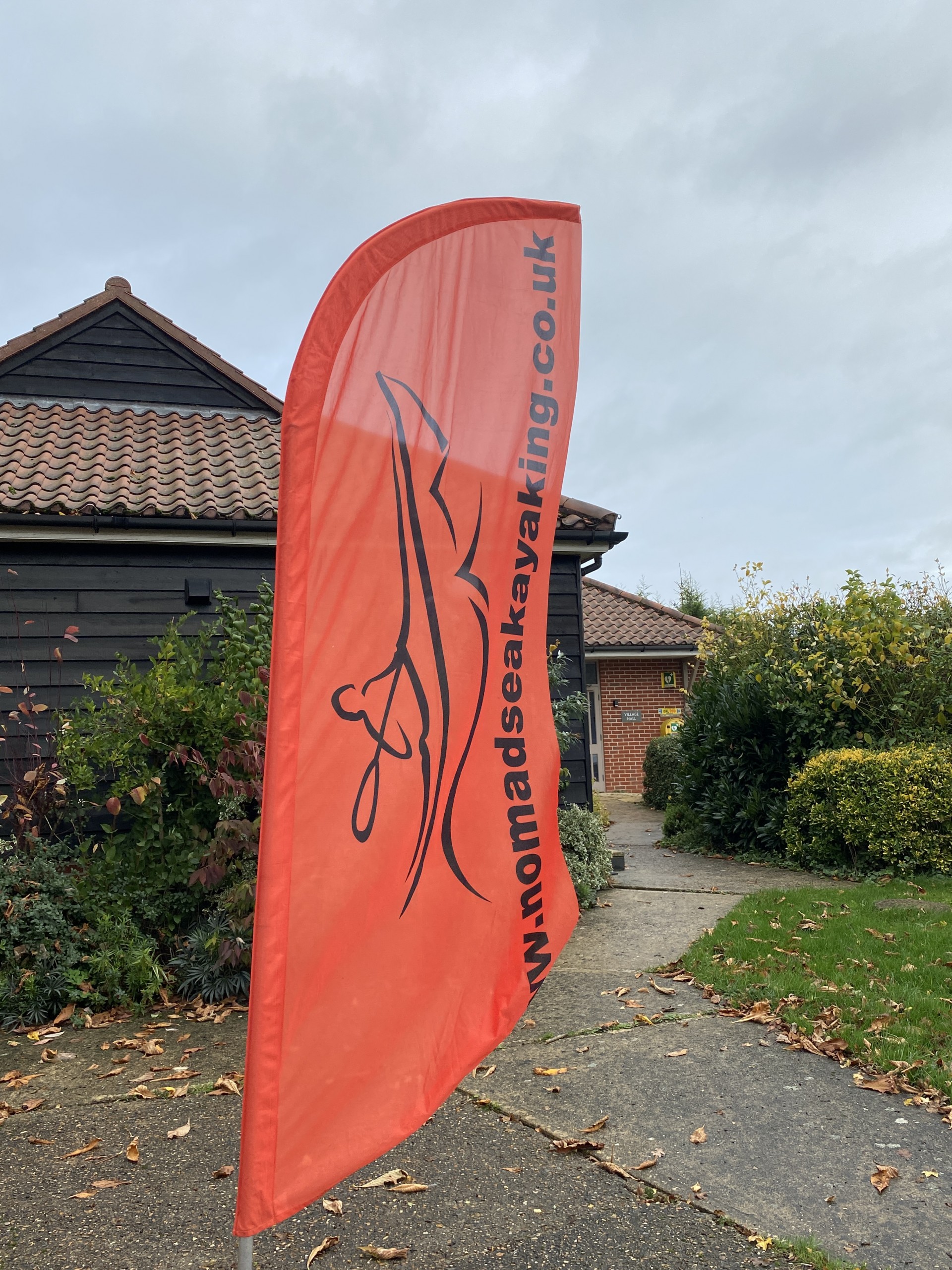 A tall orange beach flag that has NOMAD sea kayaking printed on it