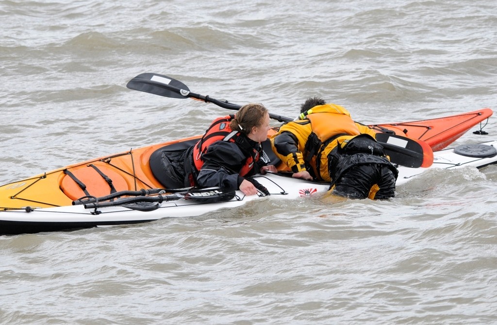 A capsized kayaker climbing back into his kayak while assisted by another kayaker