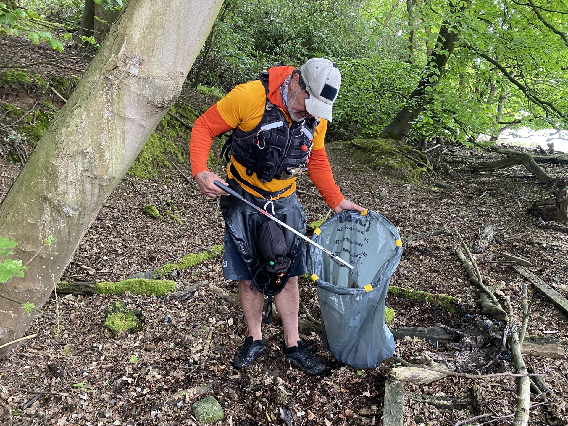 Sea kayak guide collecting refuse off a wooded beach on the Orwell estuary.