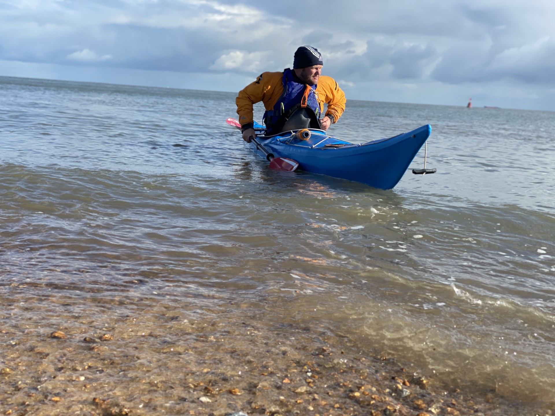Sea kayaker installing his spray deck whilst launching off a beach.