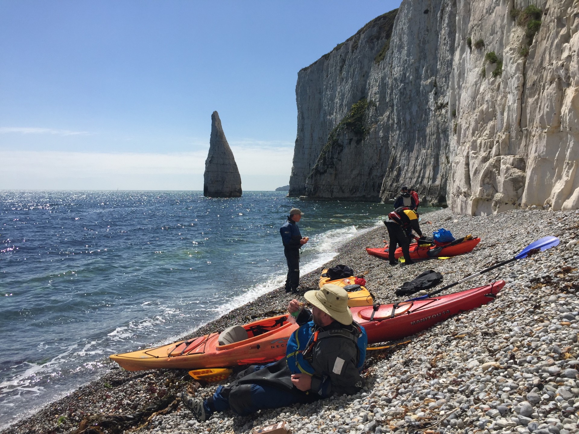 Kayakers sitting on a shingle beach near Old Harry rocks, Swanage, Dorset coast