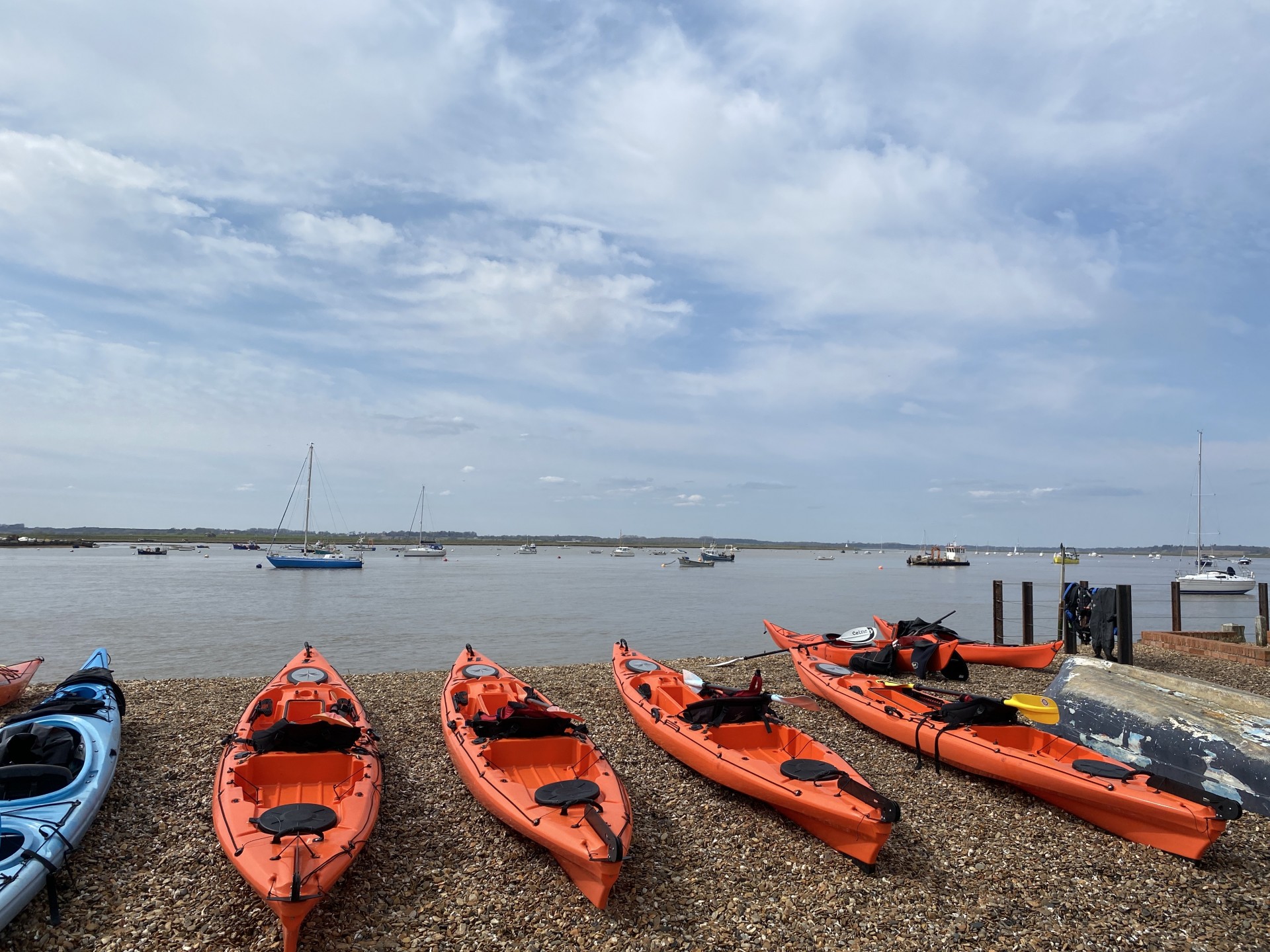 Orange sit-on-top kayaks lined up on the shingle beach at Bawdsey Quay ready to launch on the 'Discover the Deben Kayaking Trip'.
