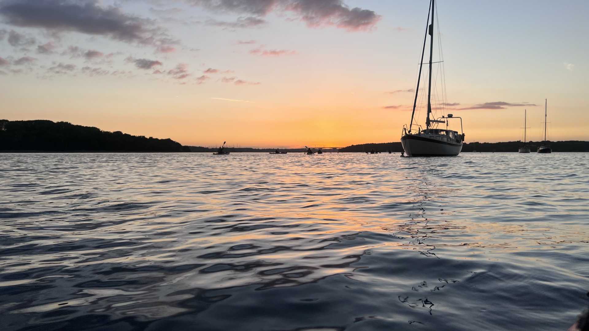 Sea kayakers in the distance passing moored yachts at sunset.