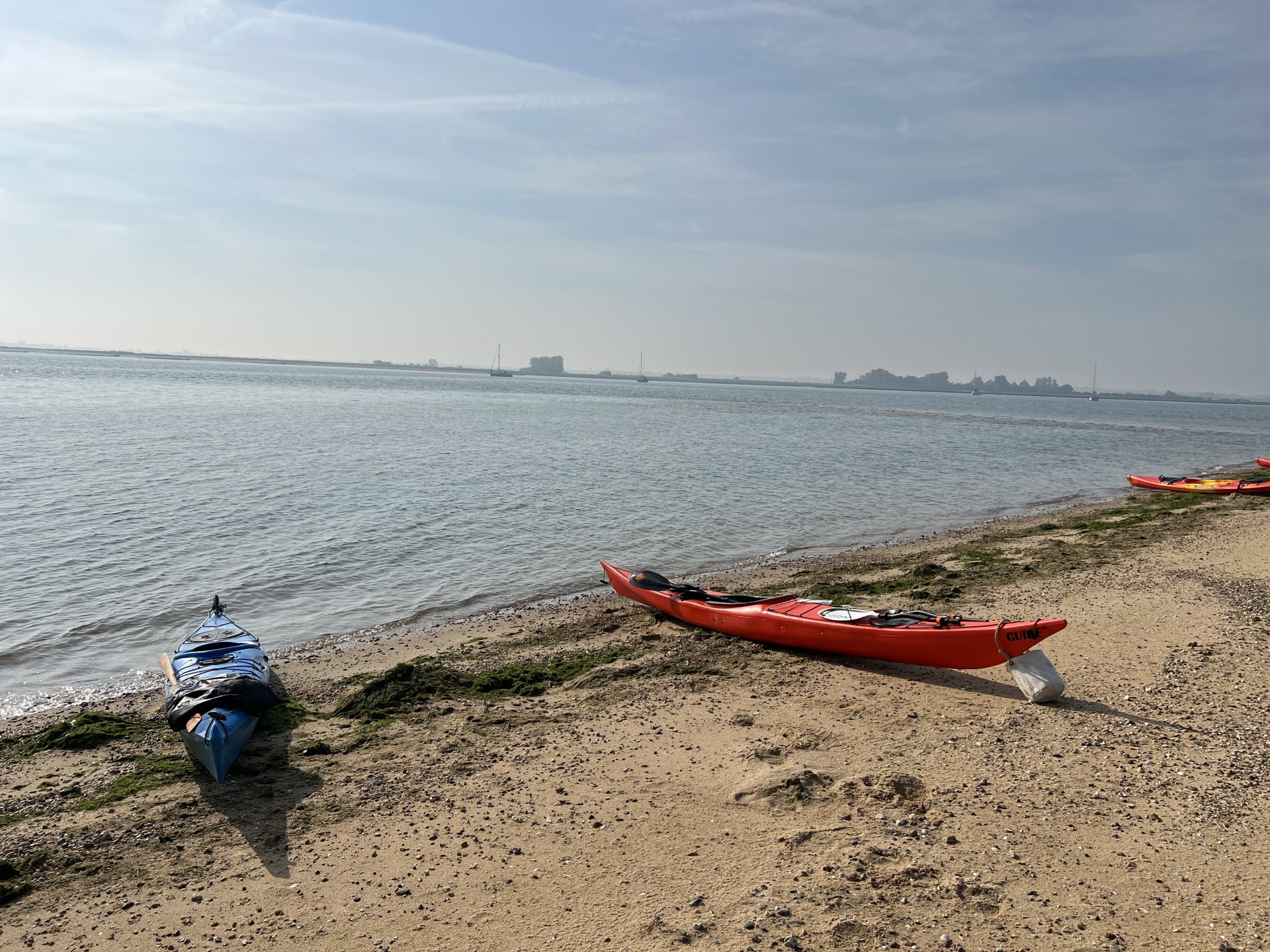 Sea kayaks on a beach with flat calm seas in background.