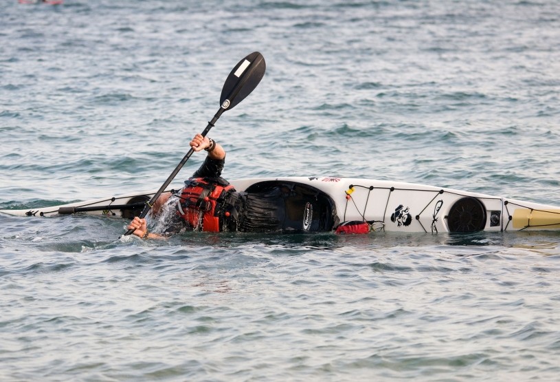 A paddler completing an eskimo roll in a sea kayak in deep tidal water.