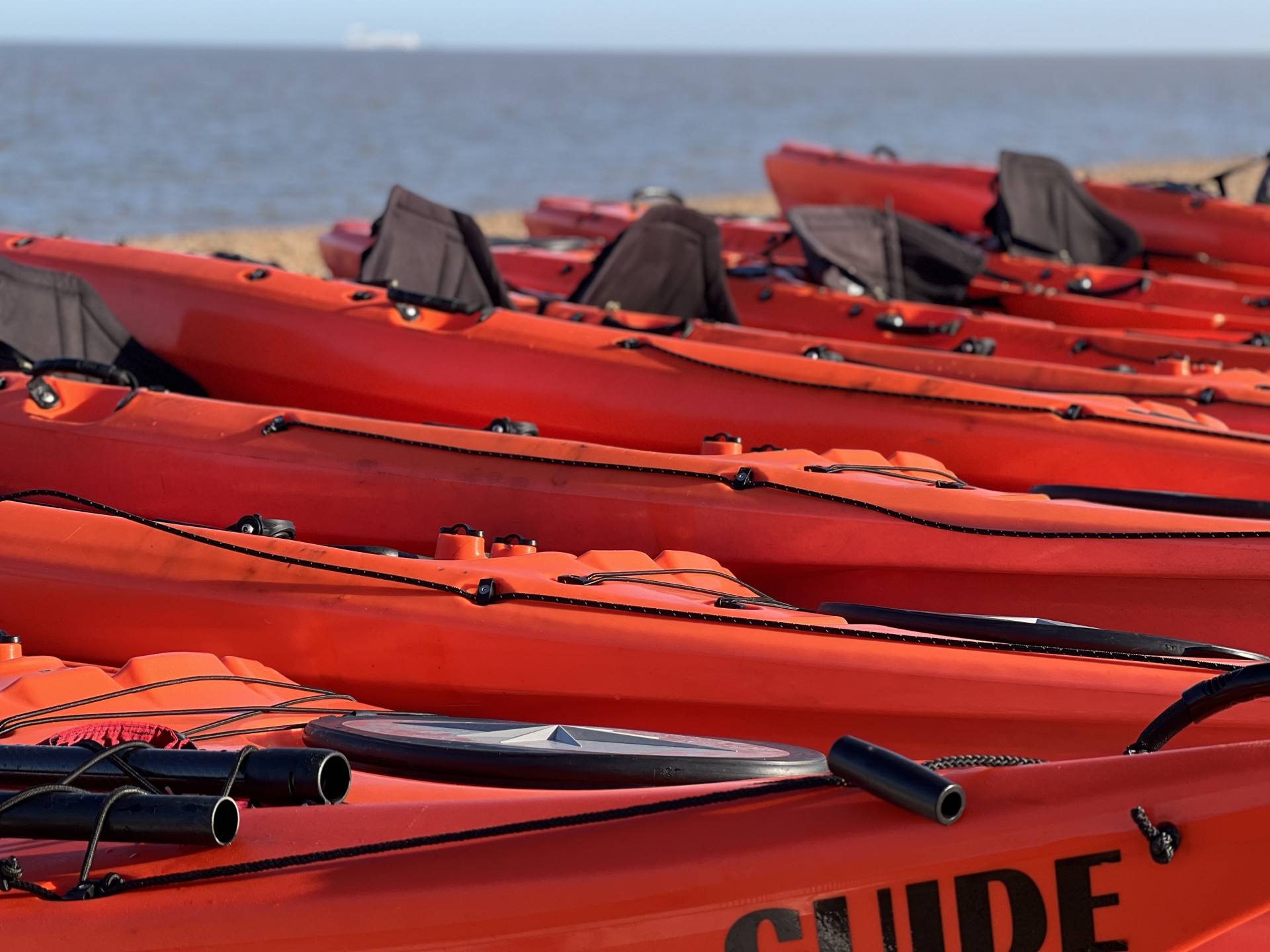 Orange kayaks on a Suffolk beach with NOMAD Sea Kayaking.