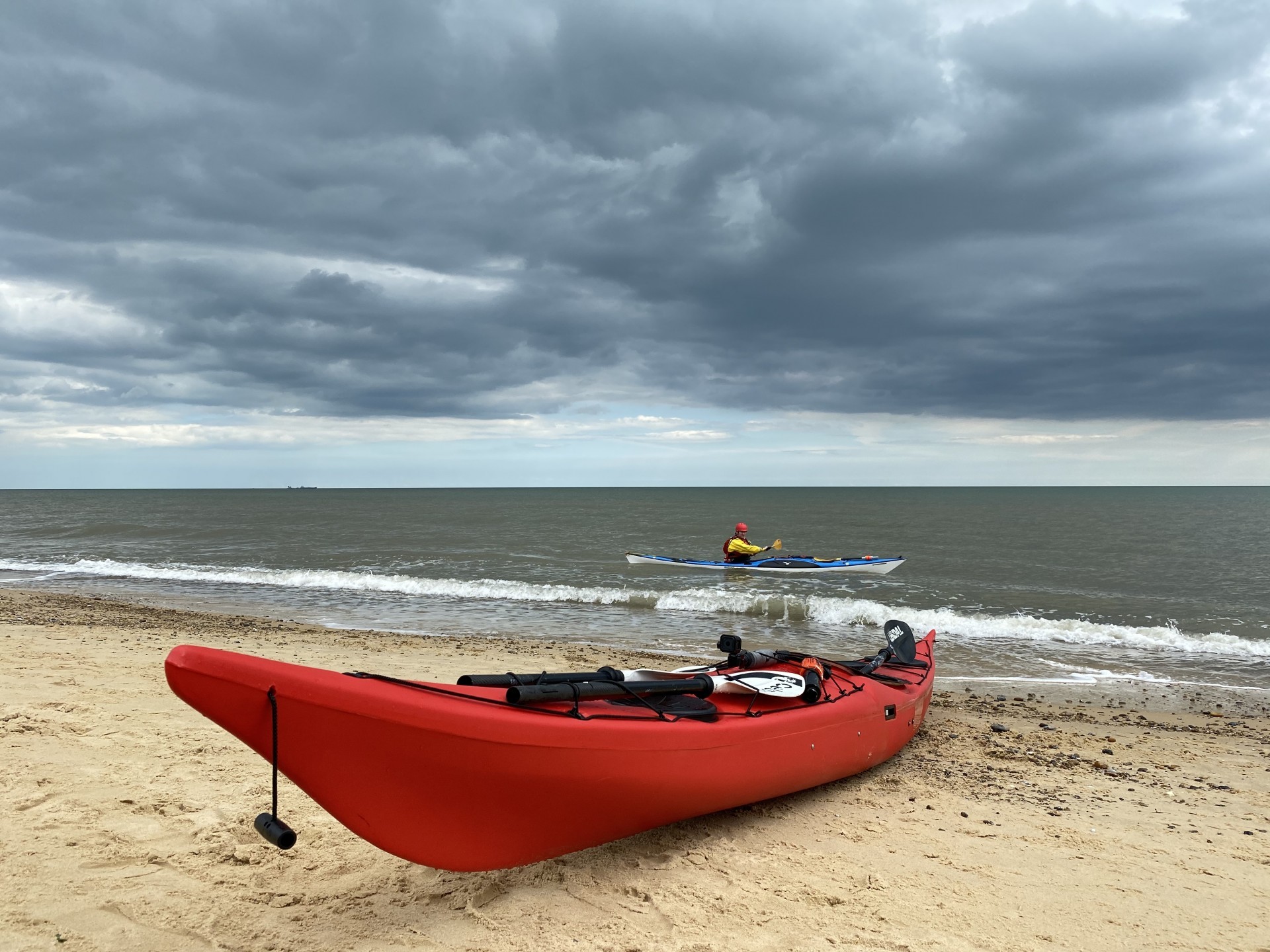 NDK RM Sport plastic sea kayak in red on a sandy beach with a paddler in the background