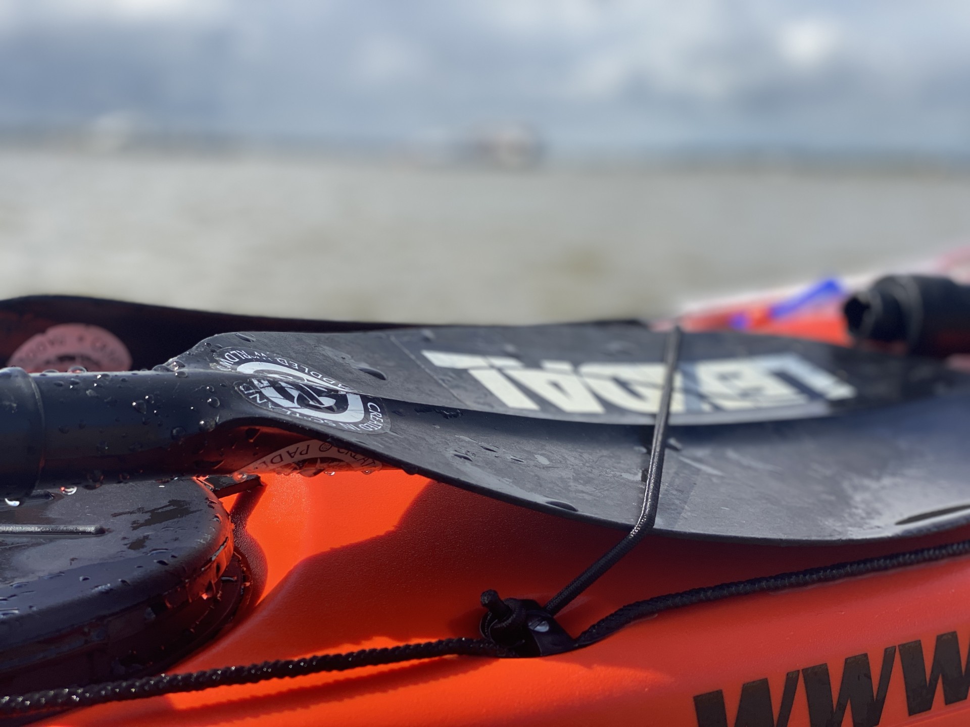 Black Lendal paddle on an orange sea kayak, NOMAD Sea Kayaking guide boat.