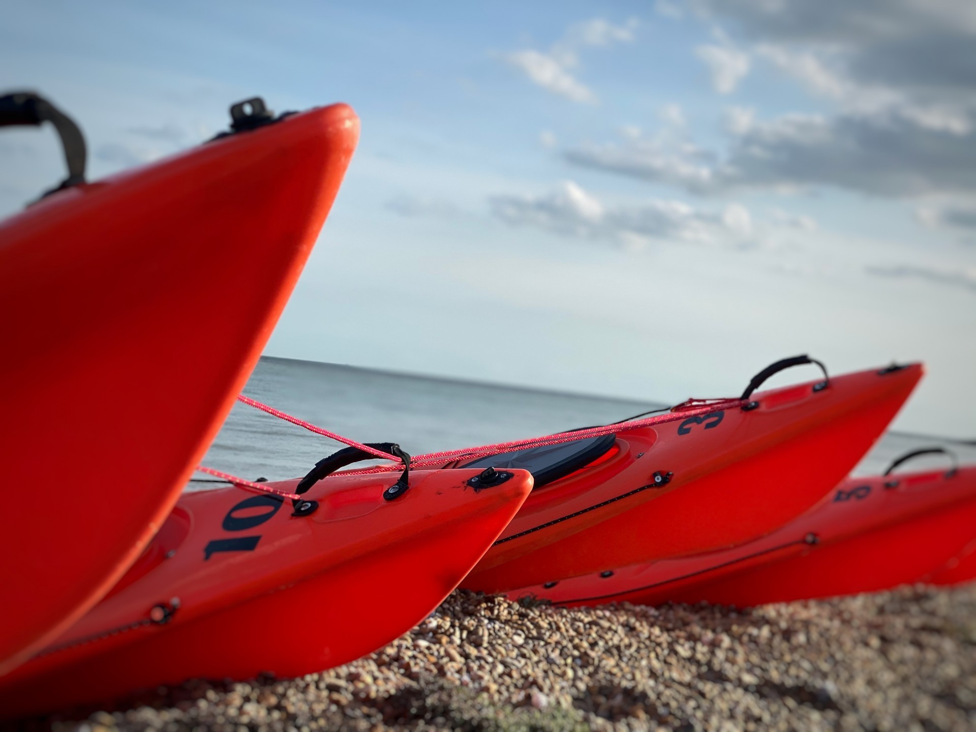 Orange kayaks on a shingle beach tethered together