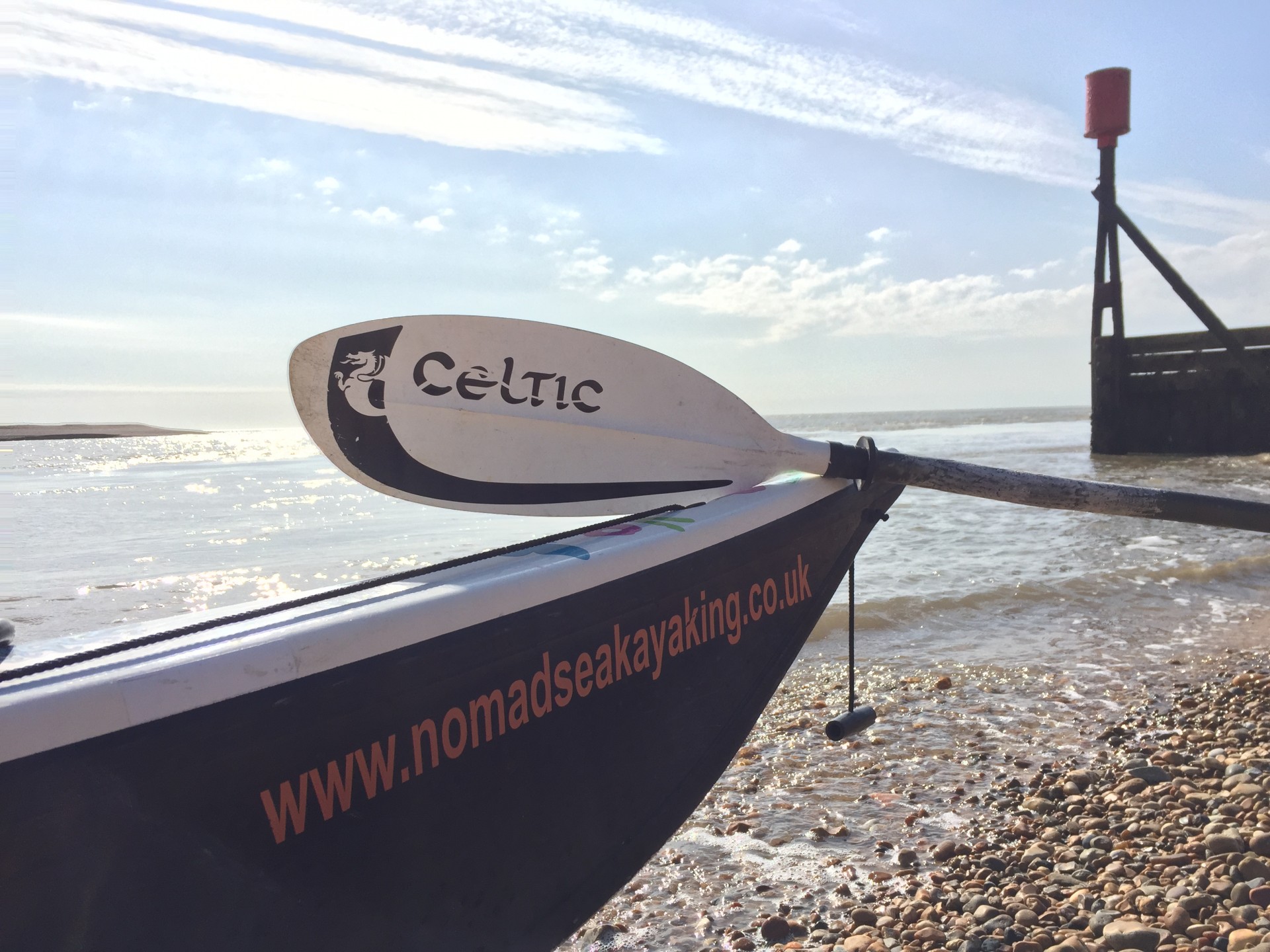 A sea kayak with the name NOMAD Sea Kayaking emblazoned on its bow.