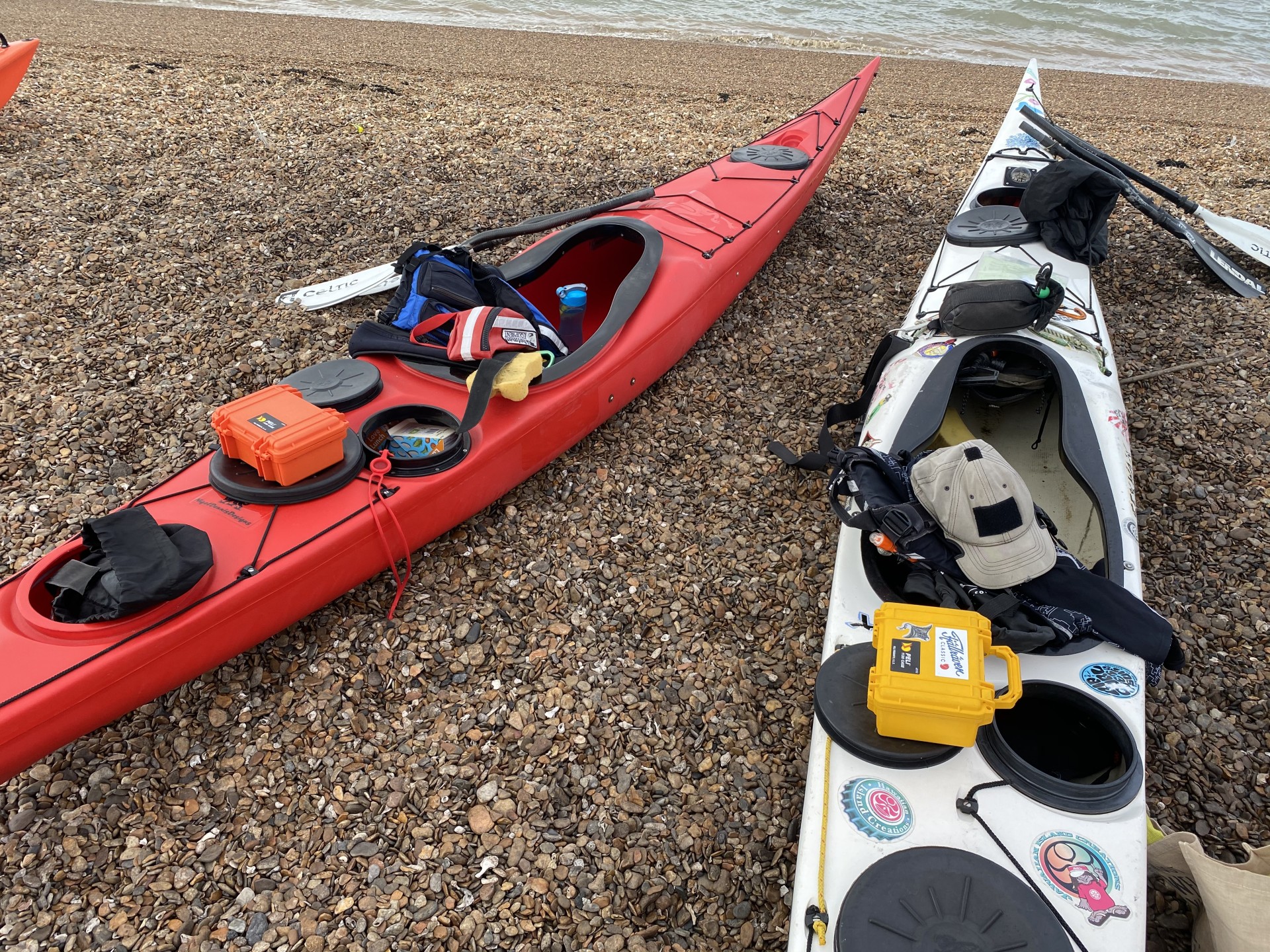 Two sea kayaks on a shingle beach in Suffolk with Peli cases on their decks.