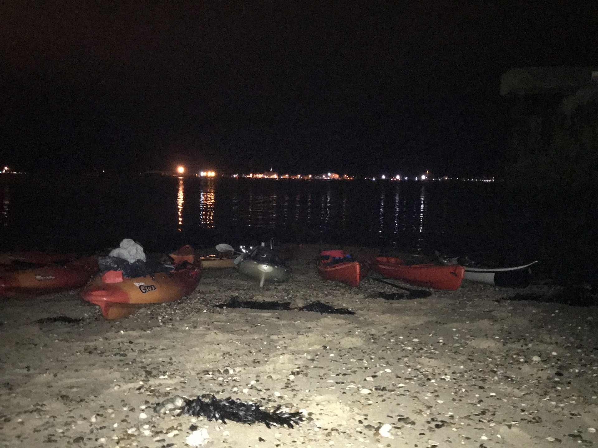 An assortment of kayaks on the beach with Harwich backlight in the distance