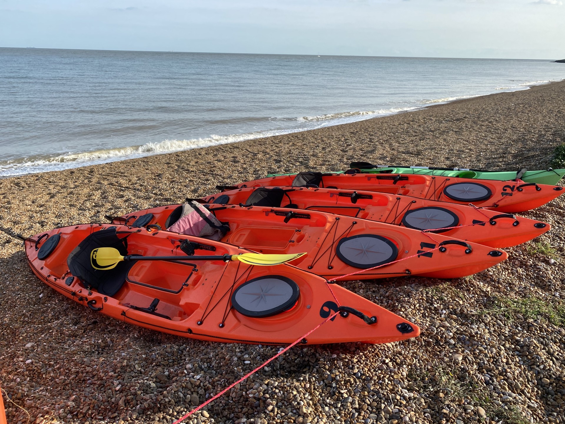 Orange fleet sit-on-top kayaks on a shingle beach in Suffolk.