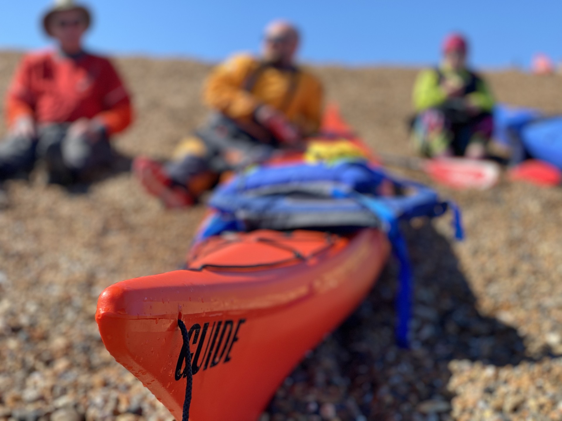 Kayakers resting on a shingle beach with a sea kayak in the foreground.