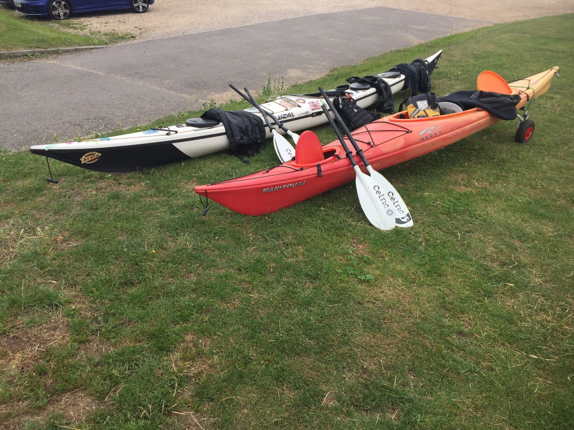 Two sea kayaks on the grass with split spare paddles.