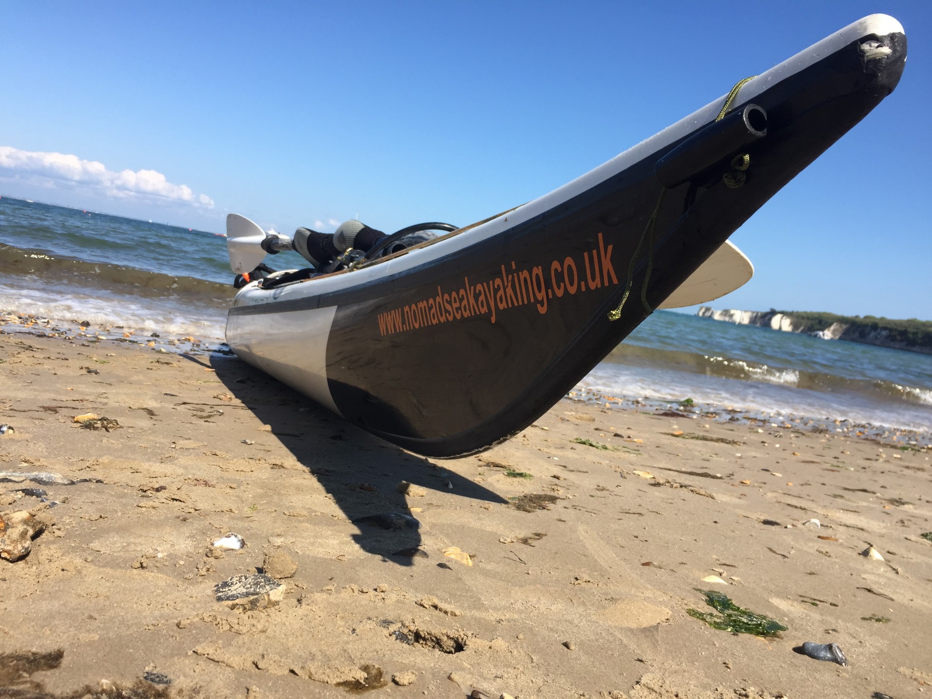 A sea kayak on a sandy beach with blue skies.