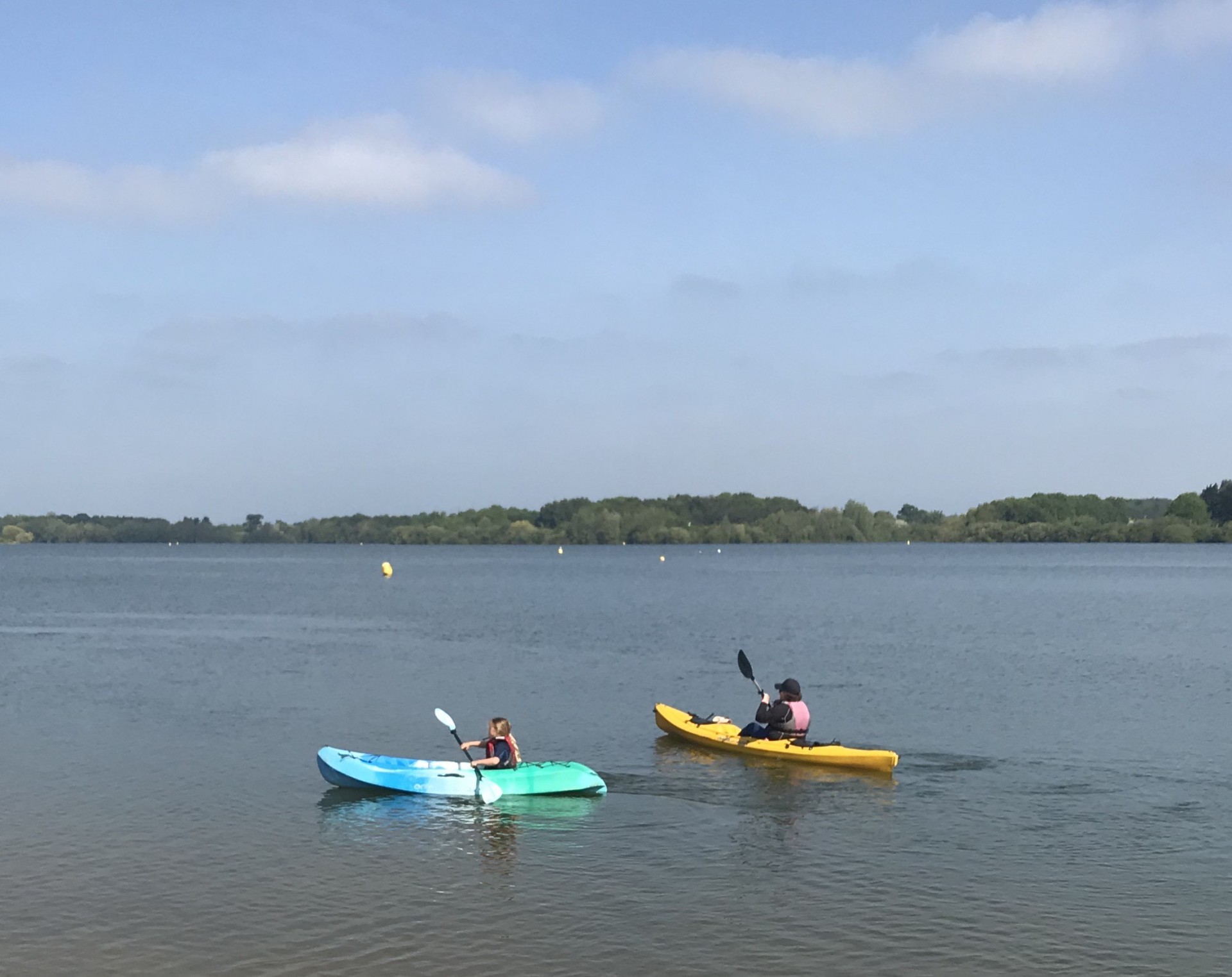 A mum and a little girl paddling kayaks on a beautiful lake on a sunny day.