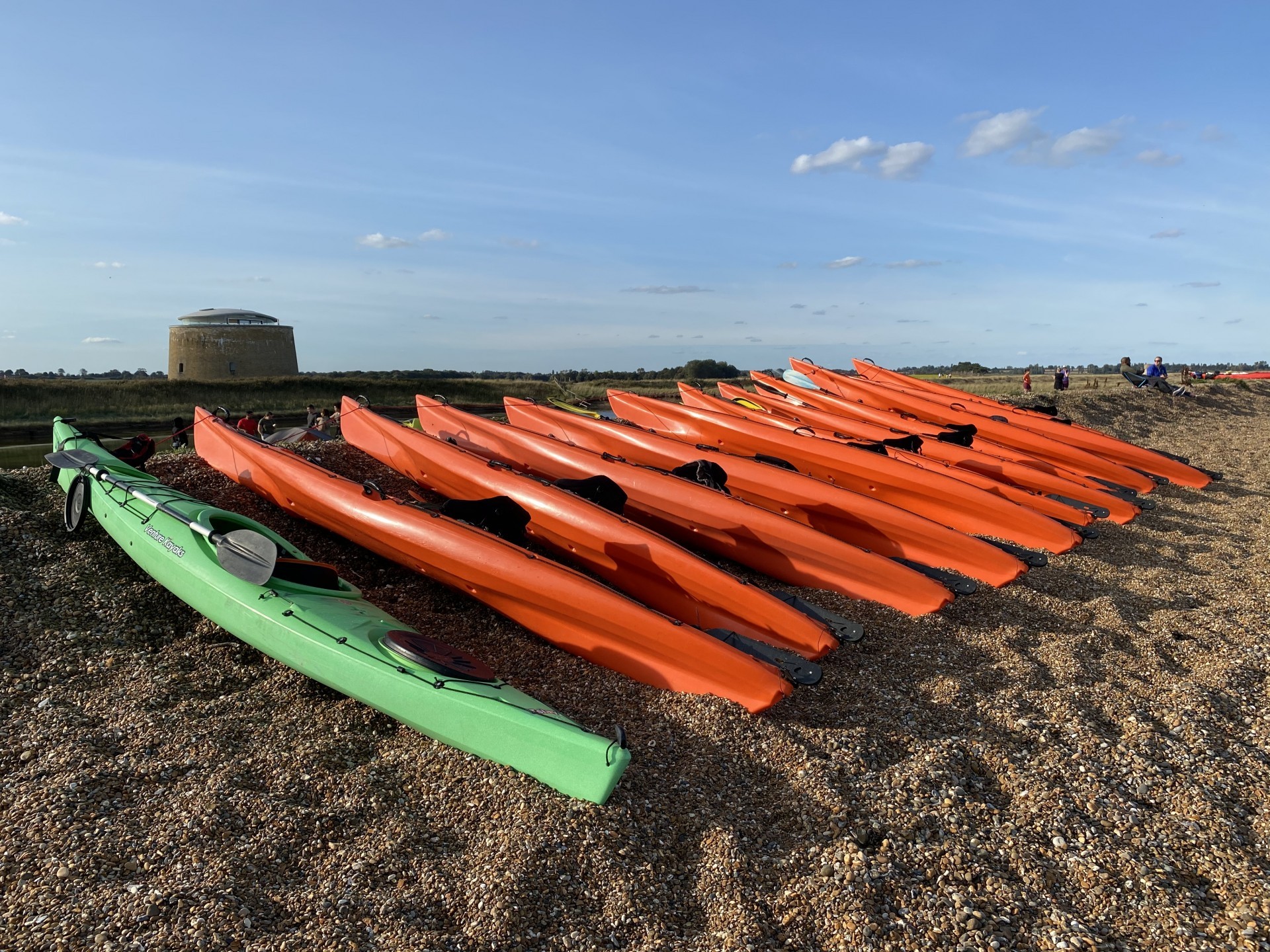 Sit-on-top and touring kayaks lines up on a shingle beach in Suffolk