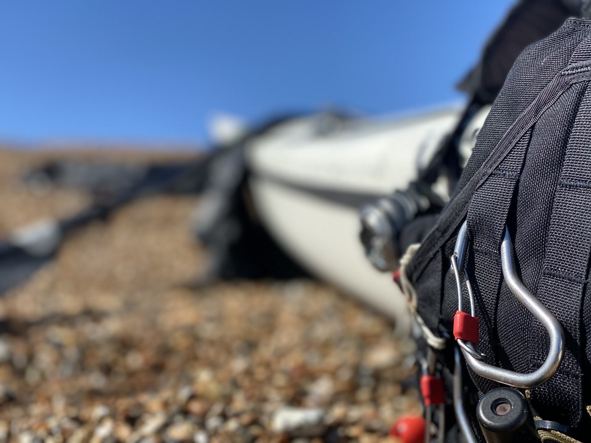 A black buoyancy aid with a carabiner and a shingle beach in the background.