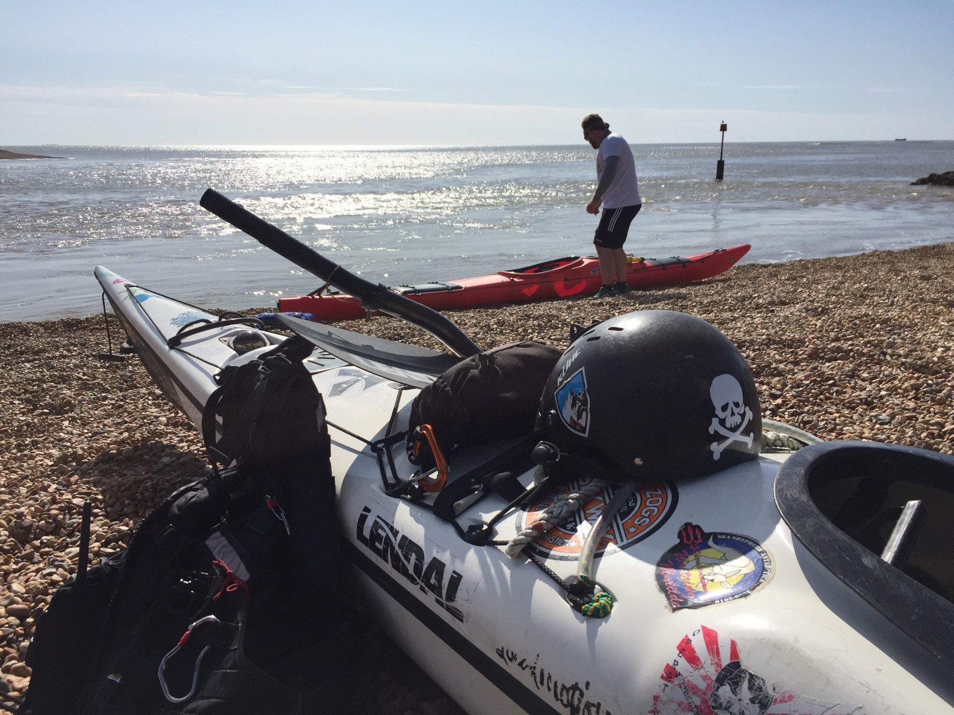 Kayaks on a shingle beach on a sunny day ready for the Intermediate sea kayaking course