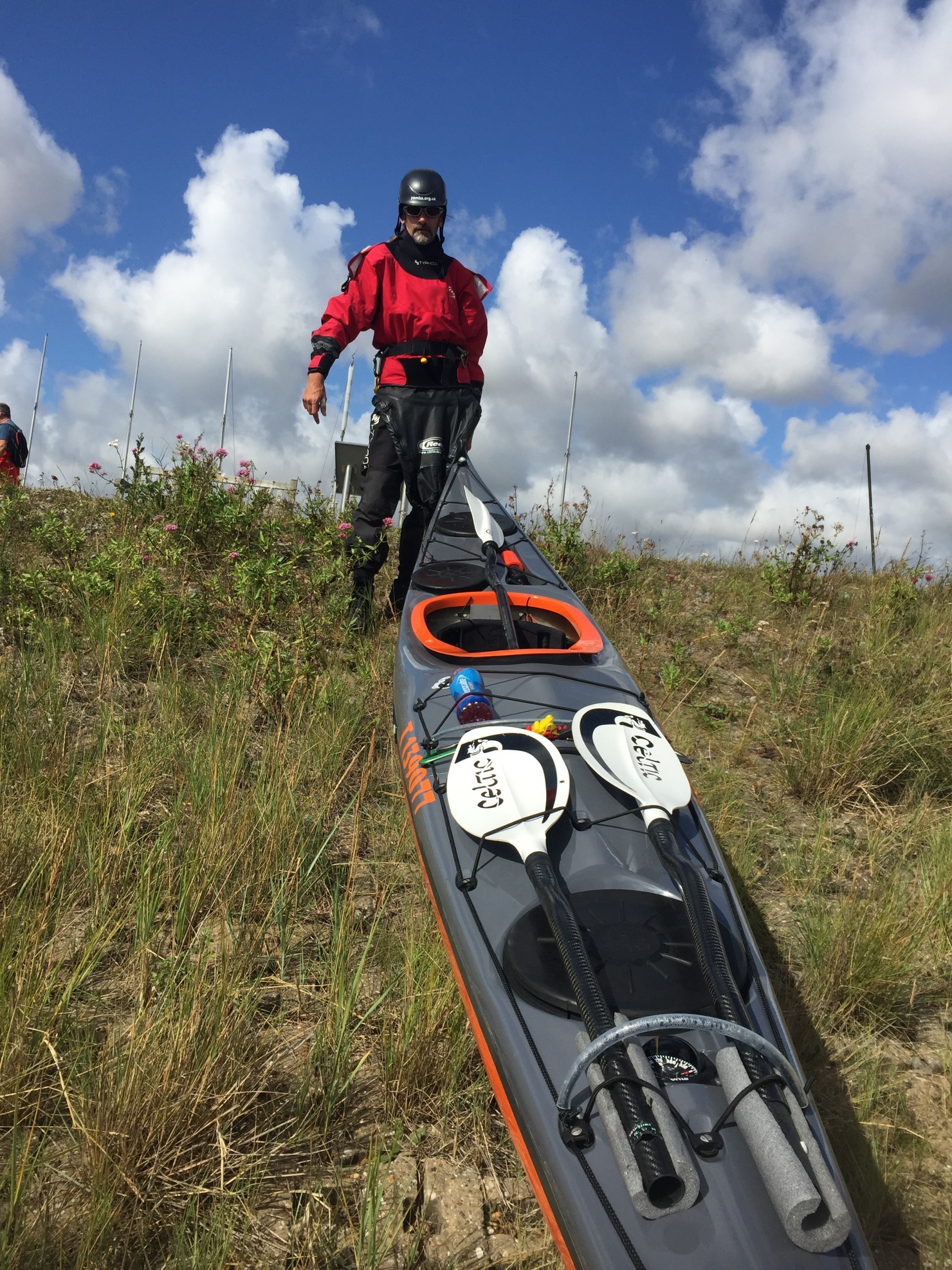 A sea kayak being carried down a grassy bank towards the ocean