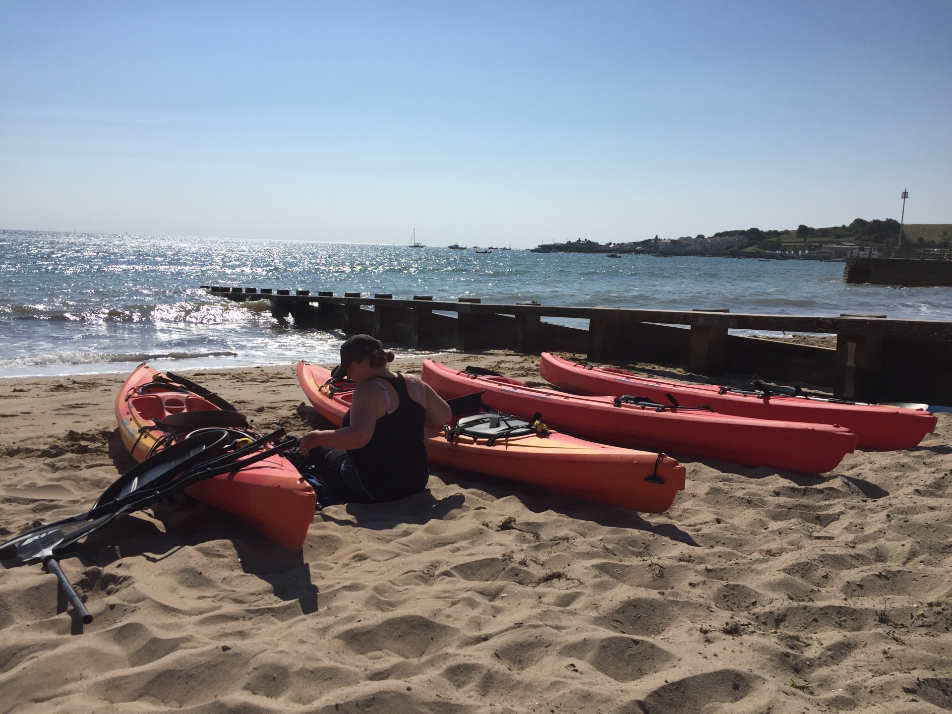 A lady sitting with her kayak pin Swanage beach with beautiful blue skies.