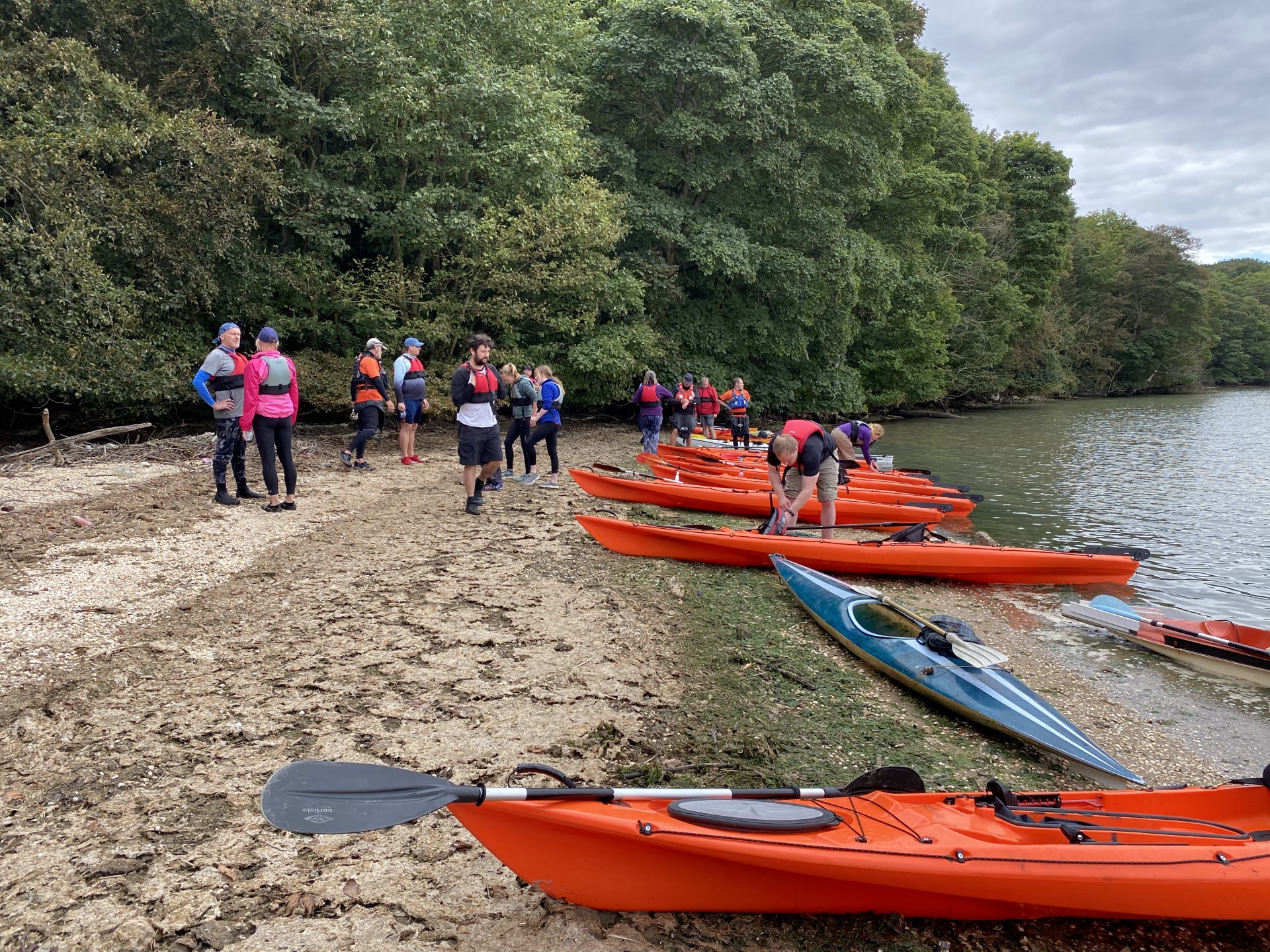 Guests on a sandy beach with sit-on-top kayaks & green treelined shore